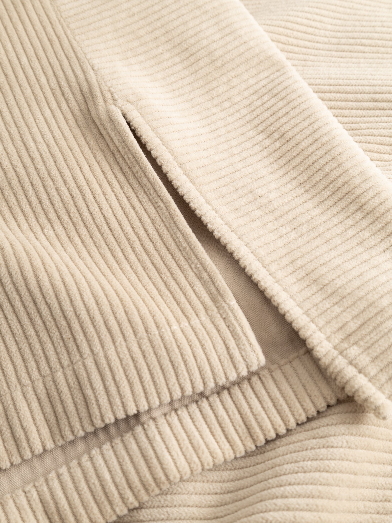 Detail close-up of the corduroy ribs and V-neck finish of the ivory vest.