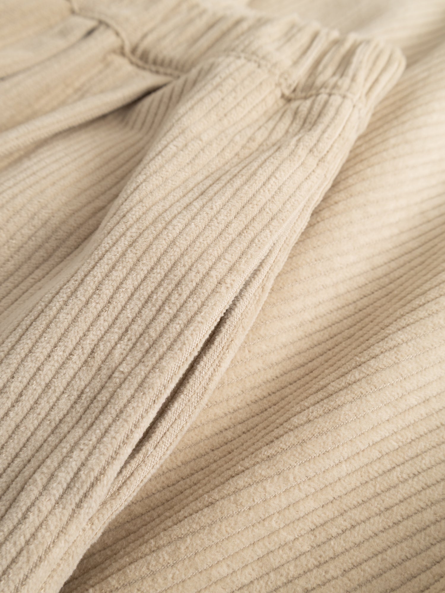 Detail close-up of the wide corduroy ribs and elastic waistband of the ivory corduroy pants.