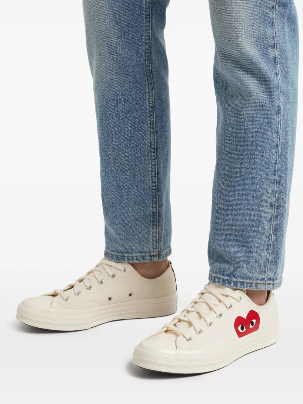 Comme des Garçons Play x Converse Chuck 70 low-top sneakers in white, model view worn with blue denim, showing red heart logo and off-white sole