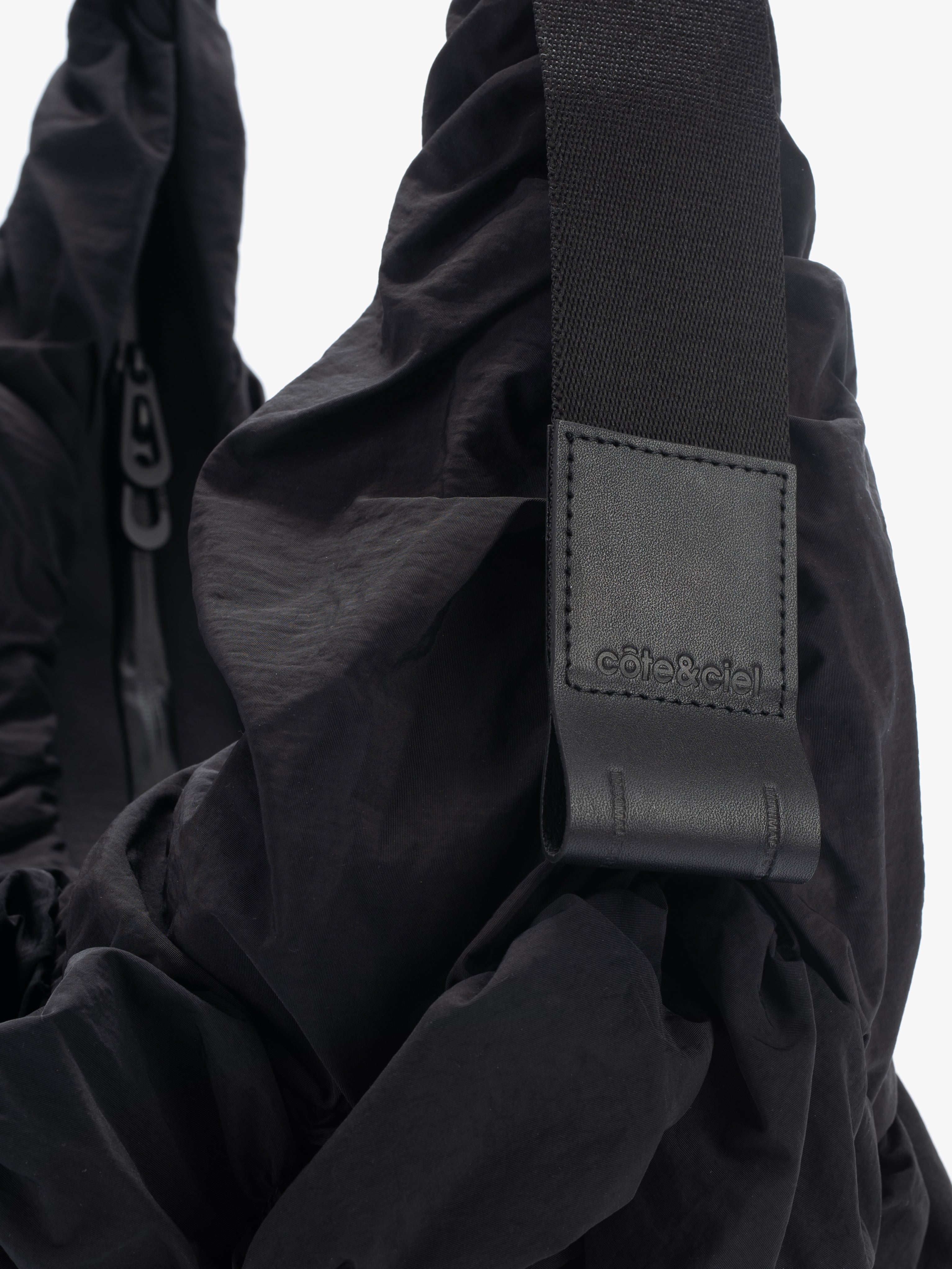 Closeup of Côte&Ciel Hyco S Otra Gathered crossbody bag in black, focusing on adjustable ergonomic strap and ring clip for accessories.