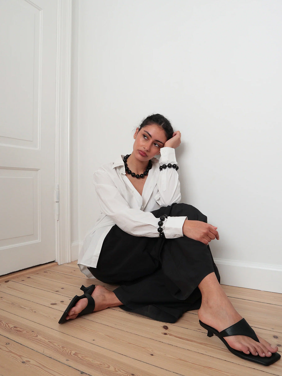 Woman sitting on a wooden floor wearing the Black and round obsidian necklace from De Silang
