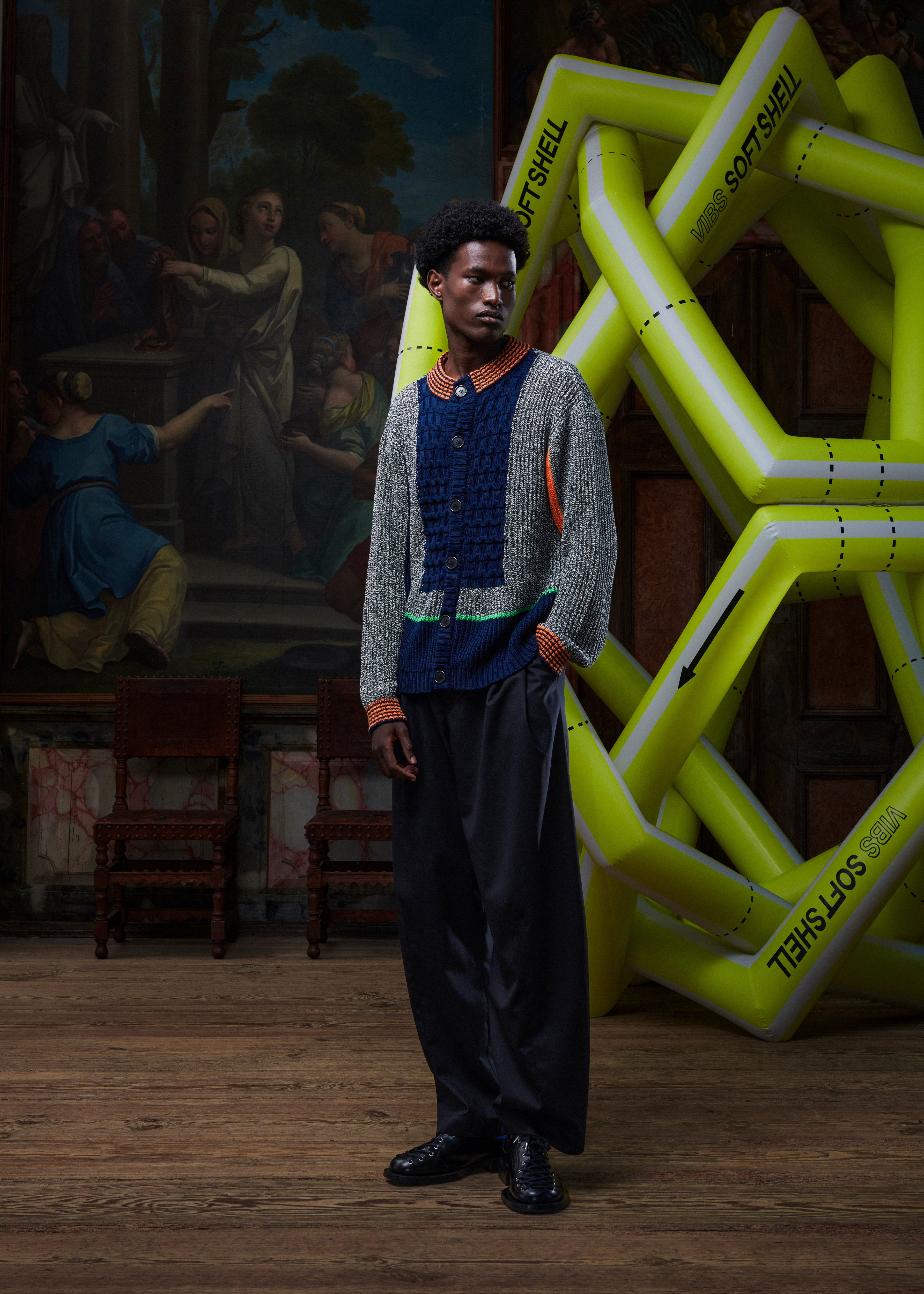 Male model wearing the Abundance Cardigan from the front, showing the unisex block design in black, white, and navy with orange accents, long sleeves, and buttoned front