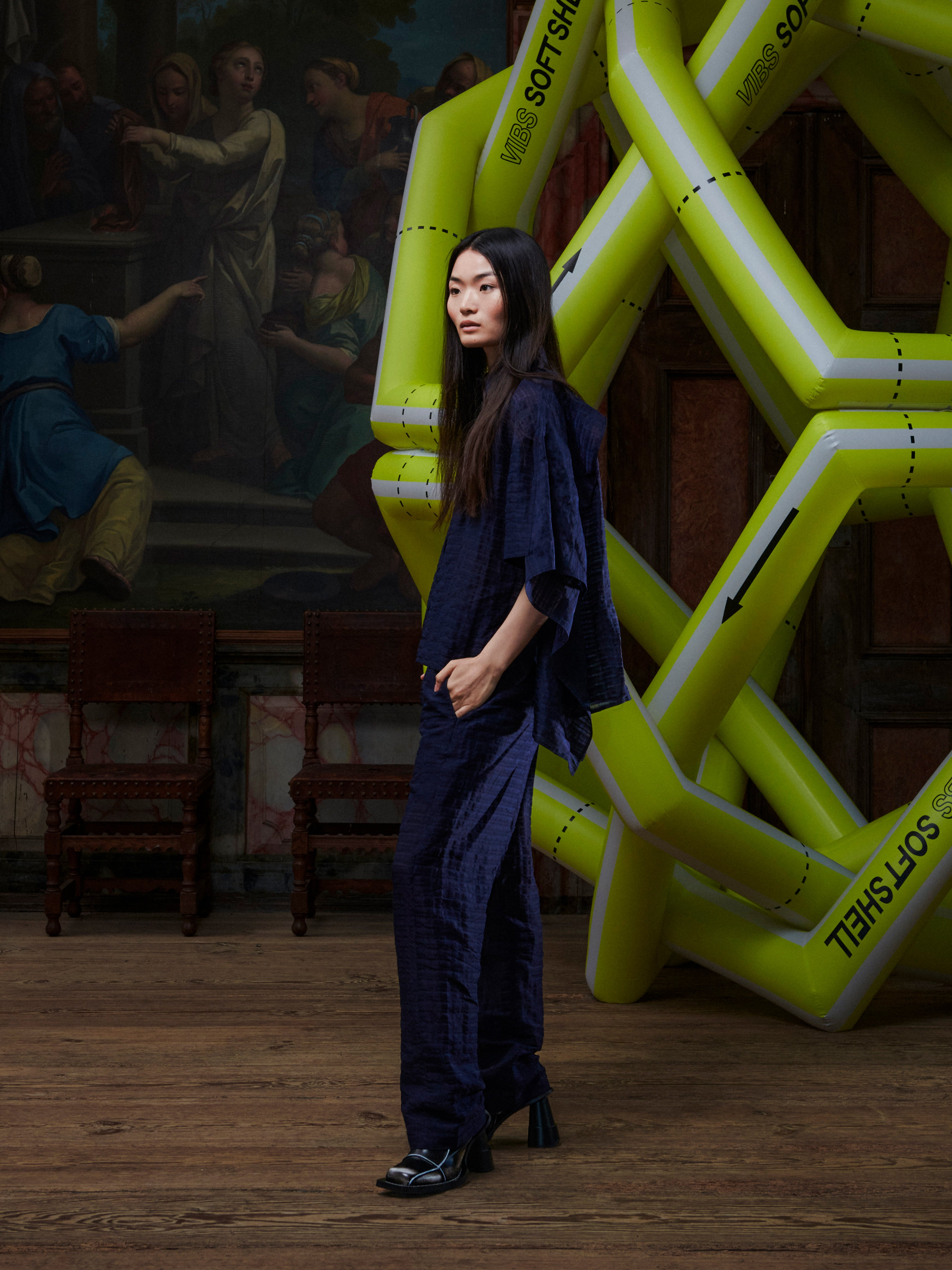 Side view of the female model wearing the Artist Pants in navy from Henrik Vibskov Spring/Summer 2026 Studio Collection, displaying the clean side profile, straight leg, and pocket design.