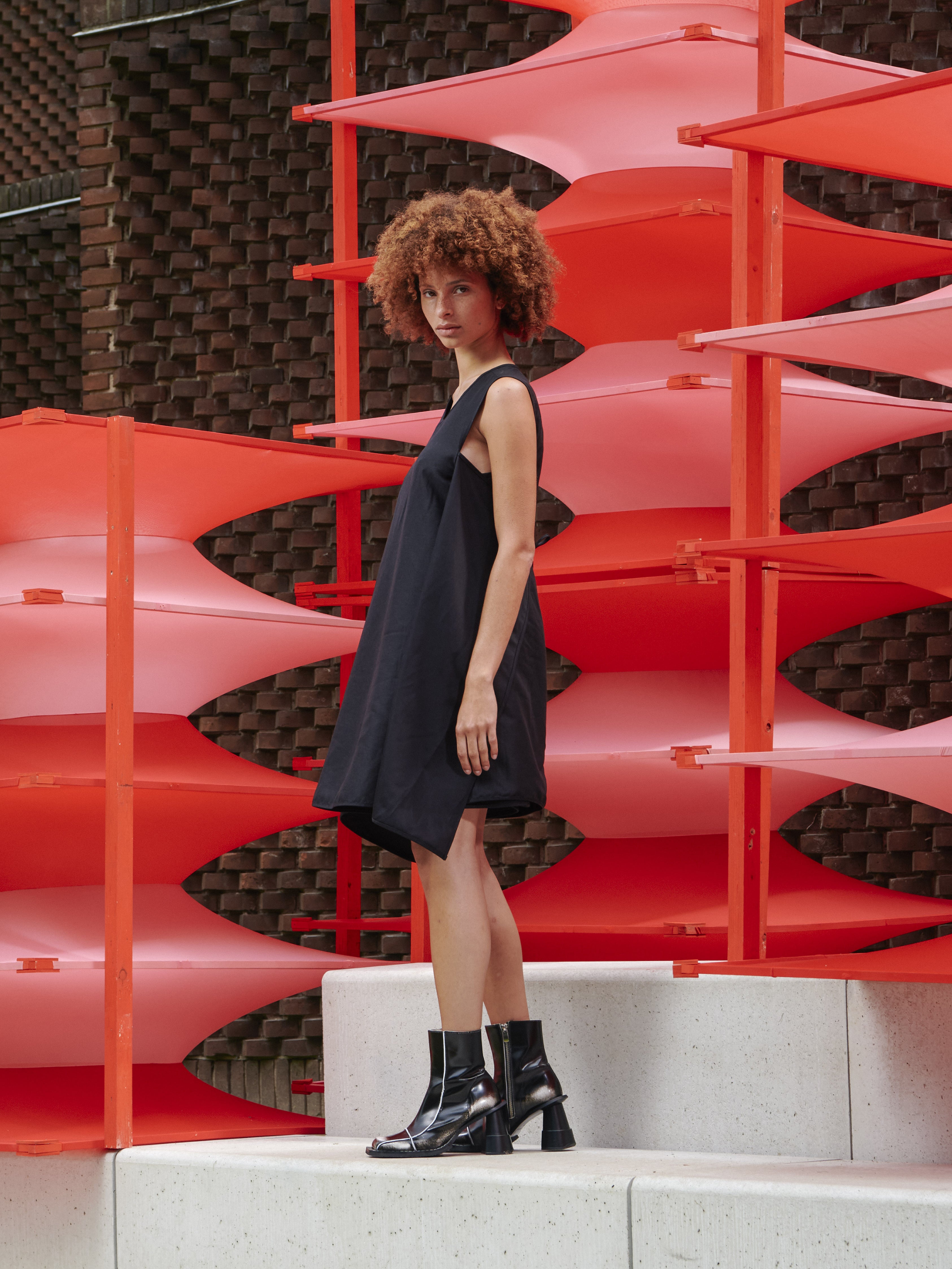 Side view of model wearing Henrik Vibskov Beetle Dress in black, styled with back tie, showing fluid drape and contemporary SS26 collection details.