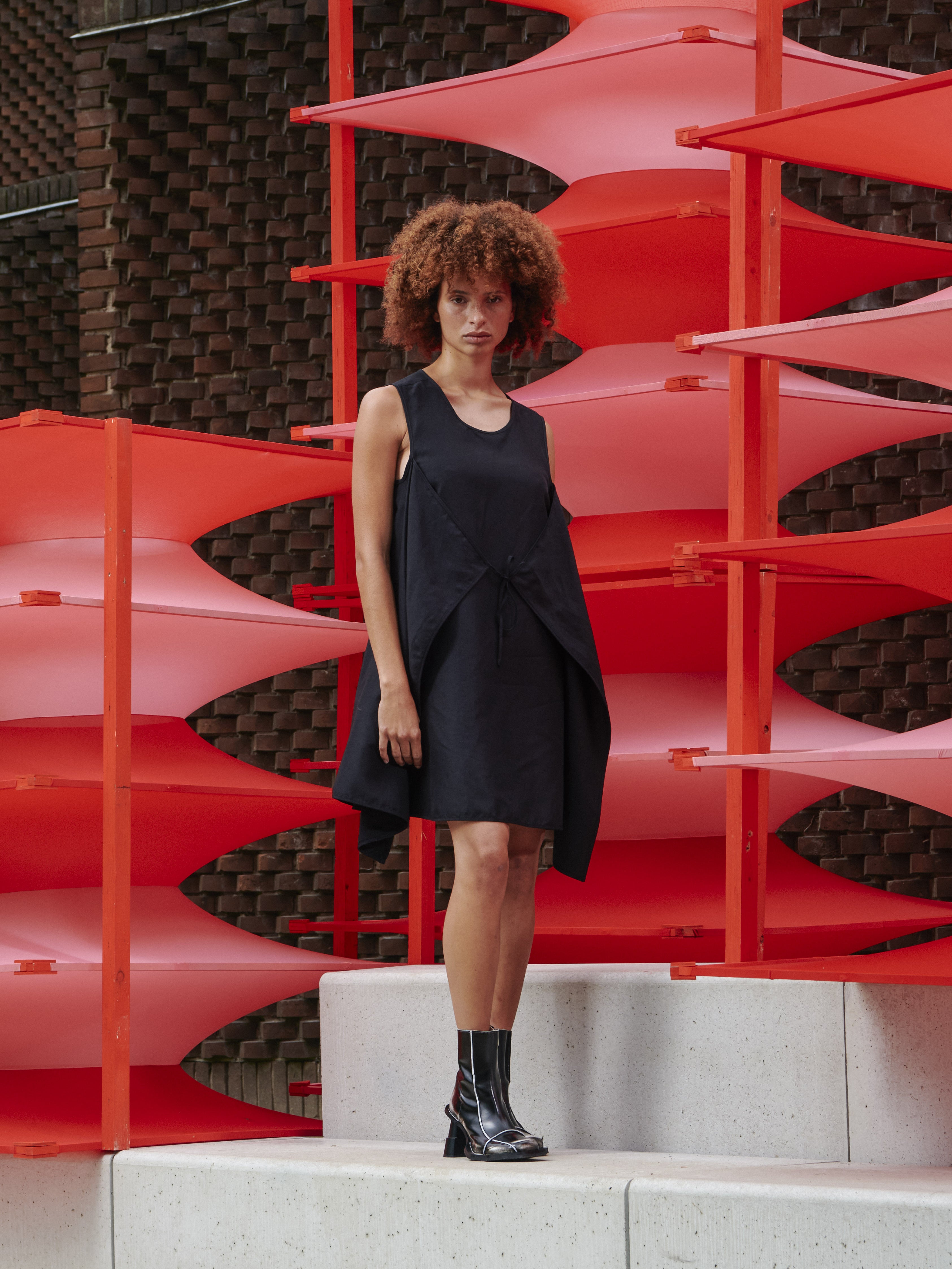 Side view of model wearing Henrik Vibskov Beetle Dress in black, styled with front tie, highlighting sculptural drape and versatile fit.