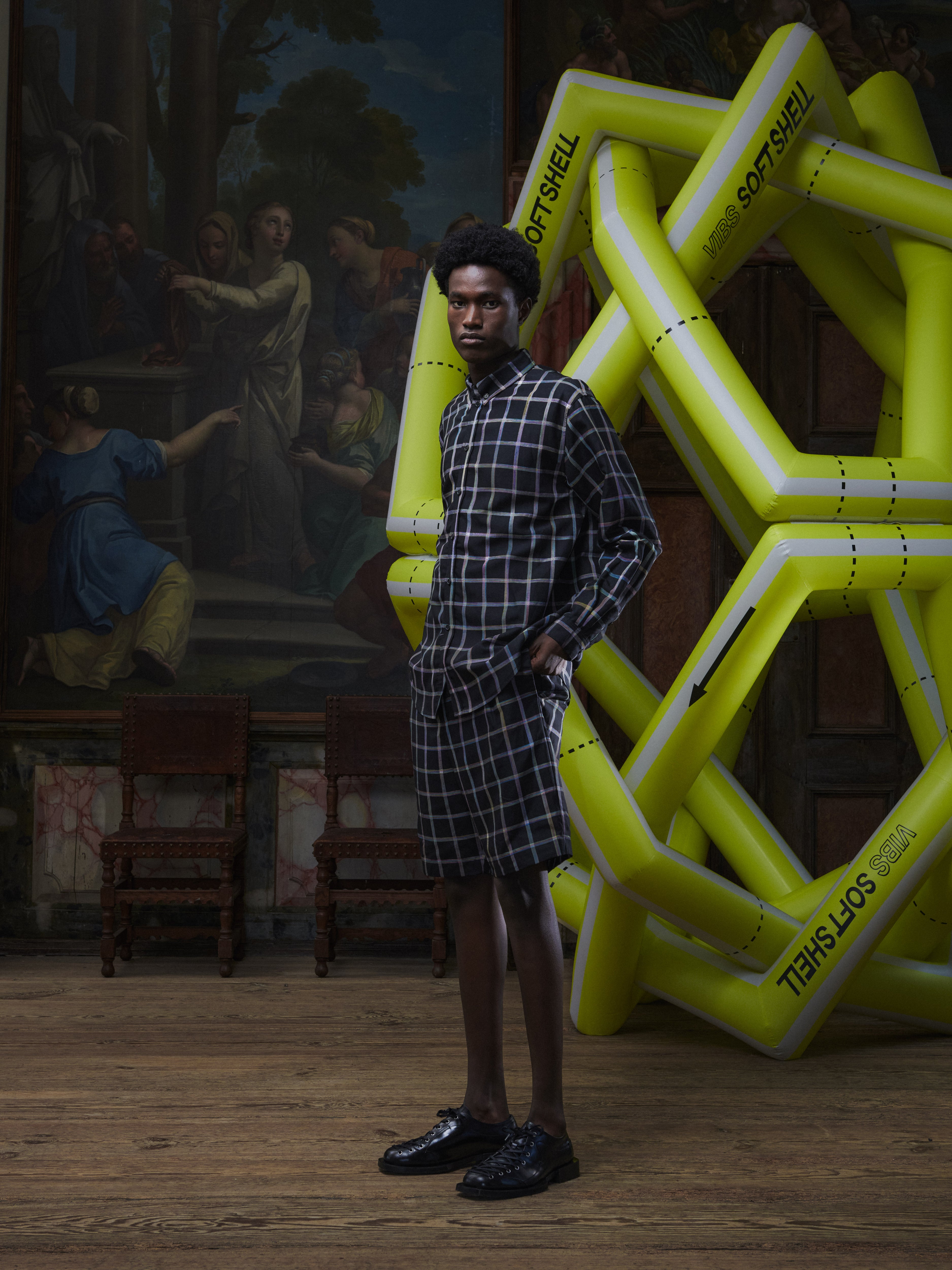 Side view of the male model wearing the Block Shirt in Black Checks from Henrik Vibskov Spring/Summer 2026 Studio Collection, displaying the shirt’s silhouette, sleeve shape, and multicoloured check pattern.