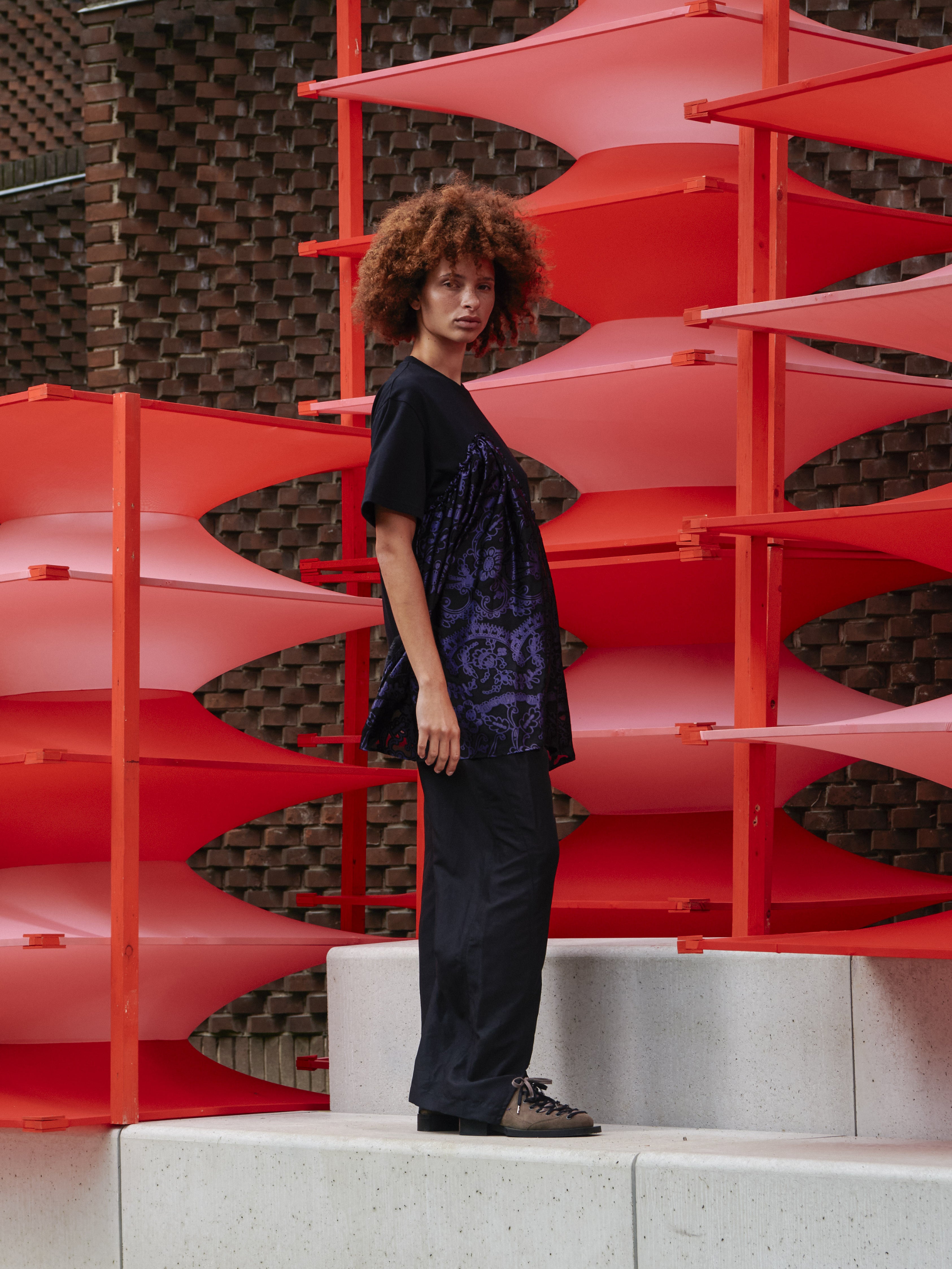 Side view of model wearing Henrik Vibskov Bon Chalant Tee in black, showing sculptural silhouette, shirt sleeves, and relaxed fit from SS26 collection.