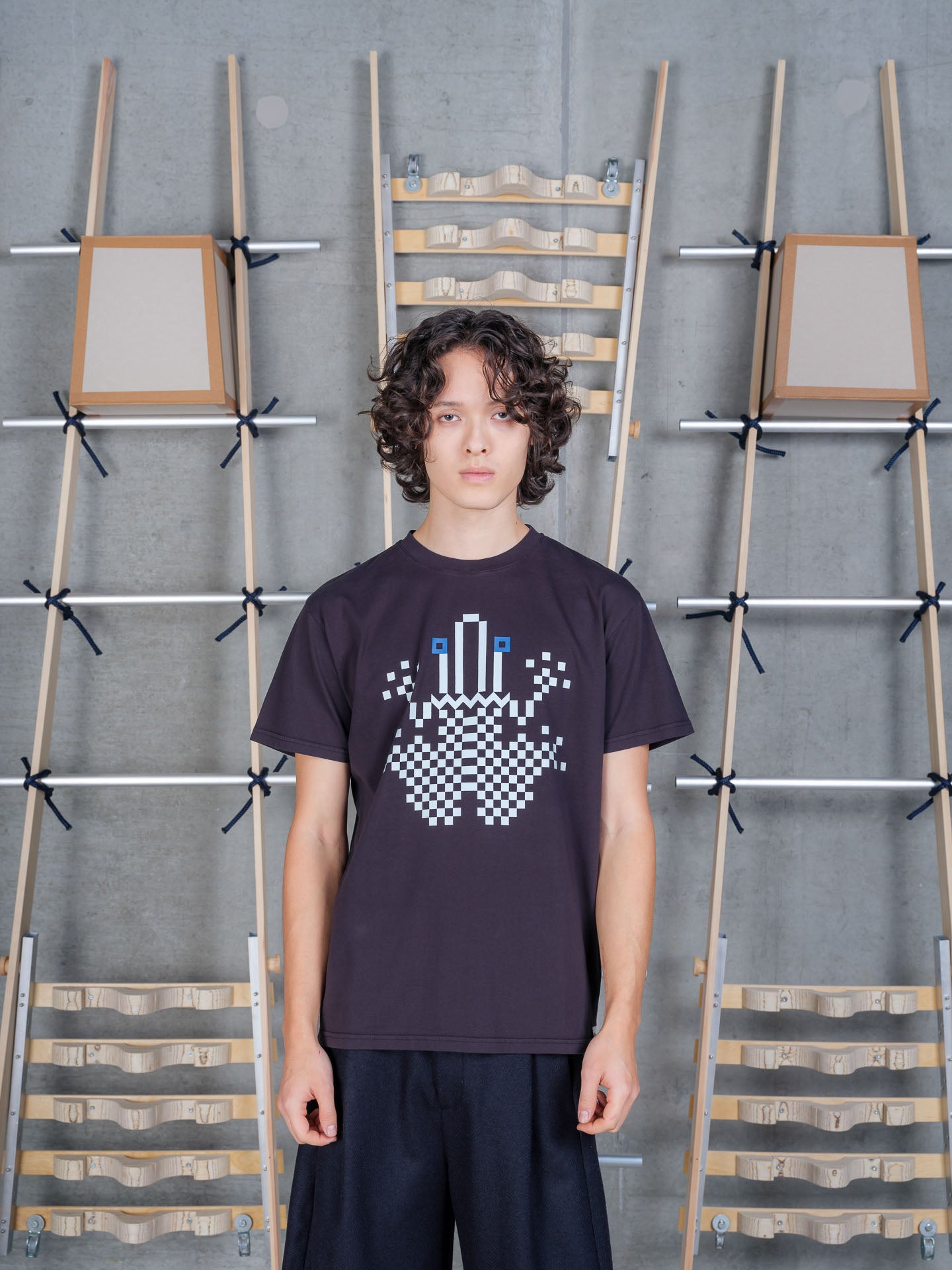 Front view of a male model wearing the Henrik Vibskov Cross Stitch Tee in Black, showcasing the pixel-inspired geometric graphic, crew neckline, and relaxed organic cotton fit