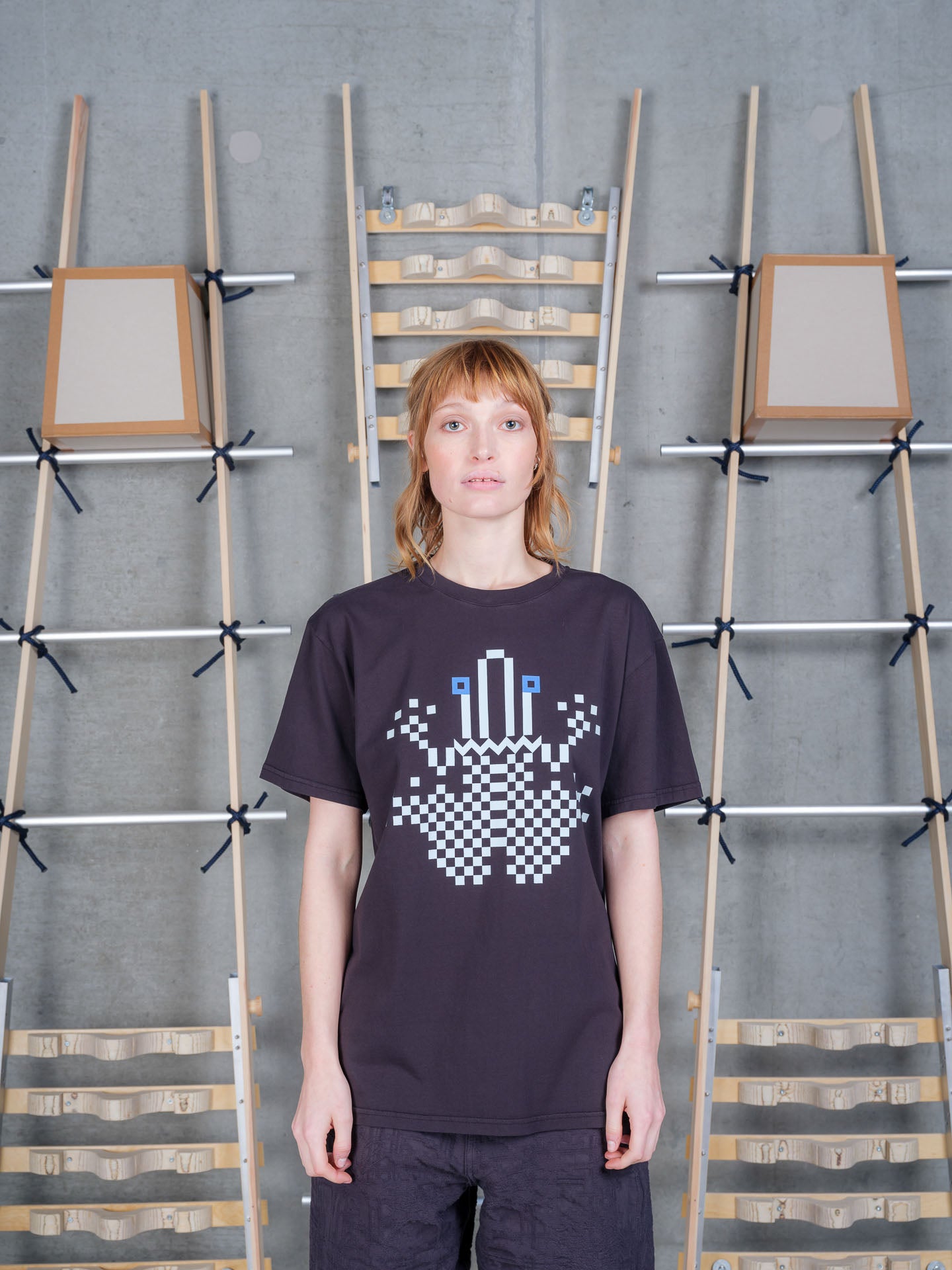 Front view of a female model wearing the Henrik Vibskov Cross Stitch Tee in Black, showing the bold cross stitch-inspired chest graphic, crew neck, and relaxed fit