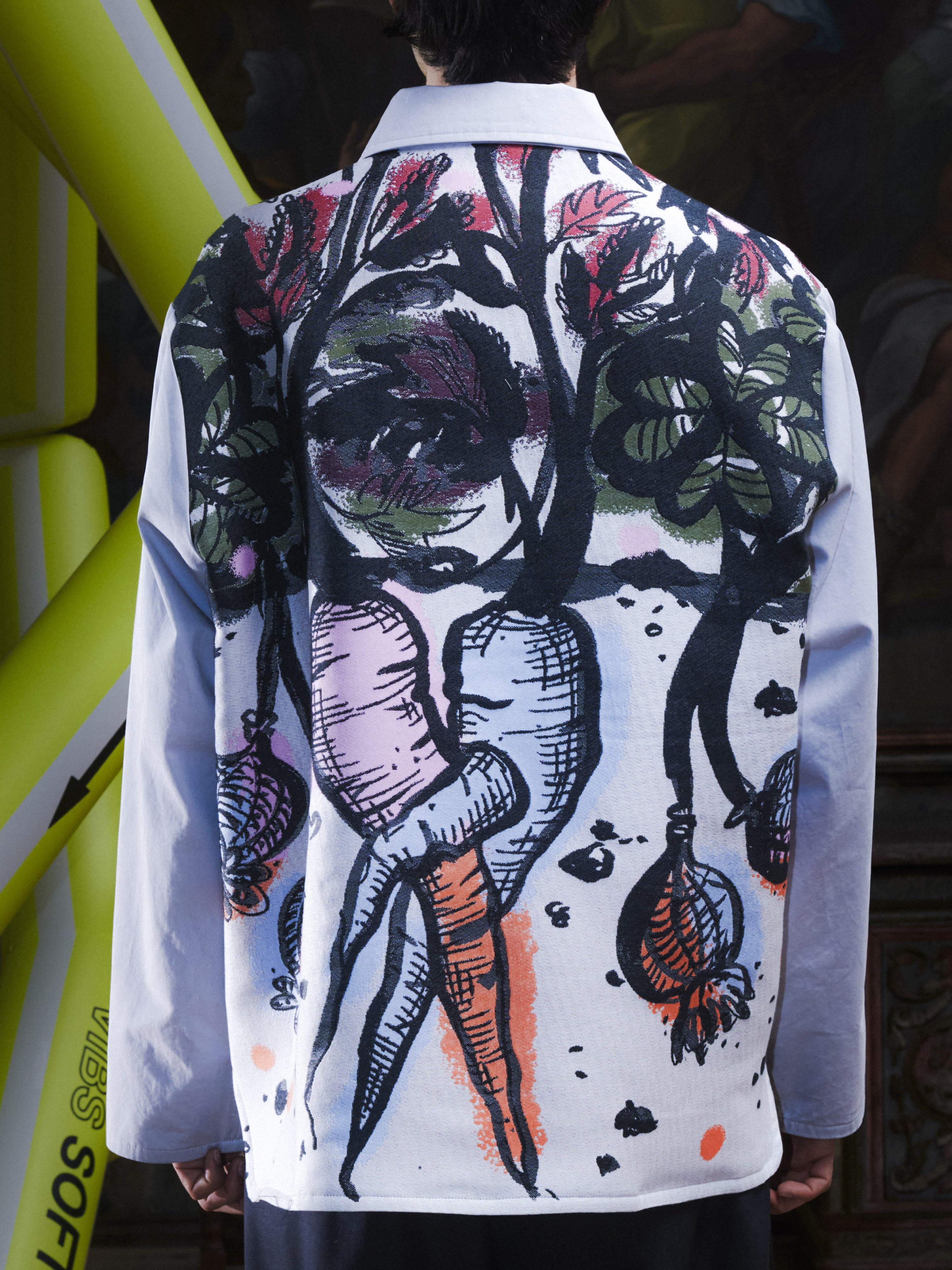 Close-up back view of the male model wearing the Care Jacket in Carrots from Henrik Vibskov Spring/Summer 2026 Studio Collection, showing the detailed multicoloured carrot pattern across the upper back.