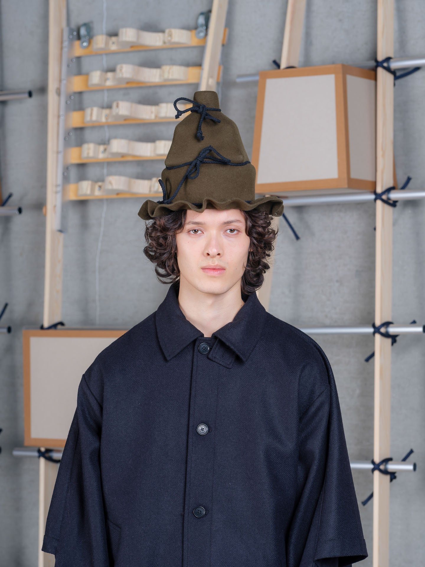 Model wearing Henrik Vibskov Christo Wrap Hat in moss green wool with layered crown and sculptural wrapped silhouette
