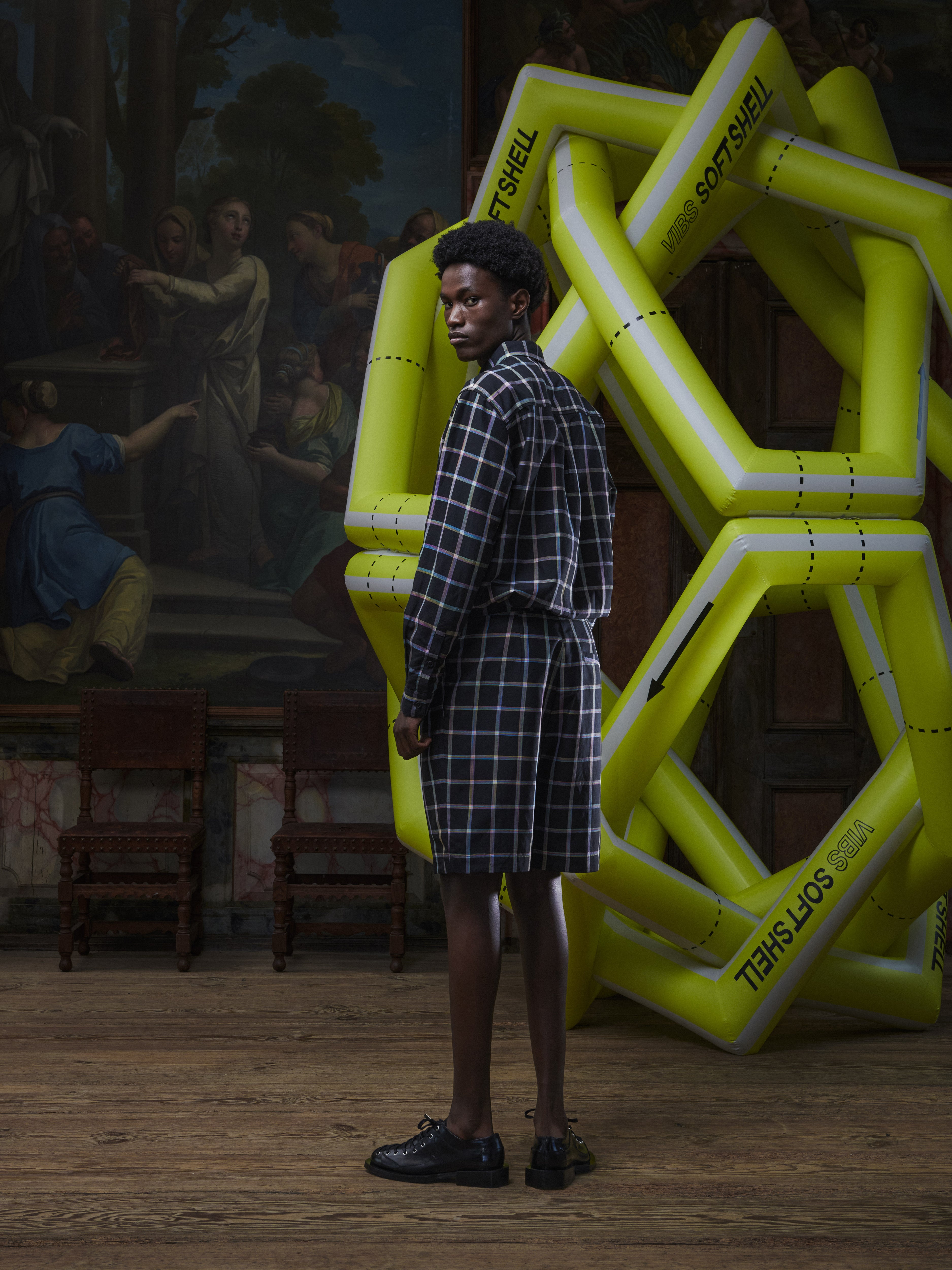 Side view of a male model wearing the Claus Shorts in Black Checks from Henrik Vibskov Spring/Summer 2026 Studio Collection, highlighting the side pockets, check pattern, and straight silhouette.