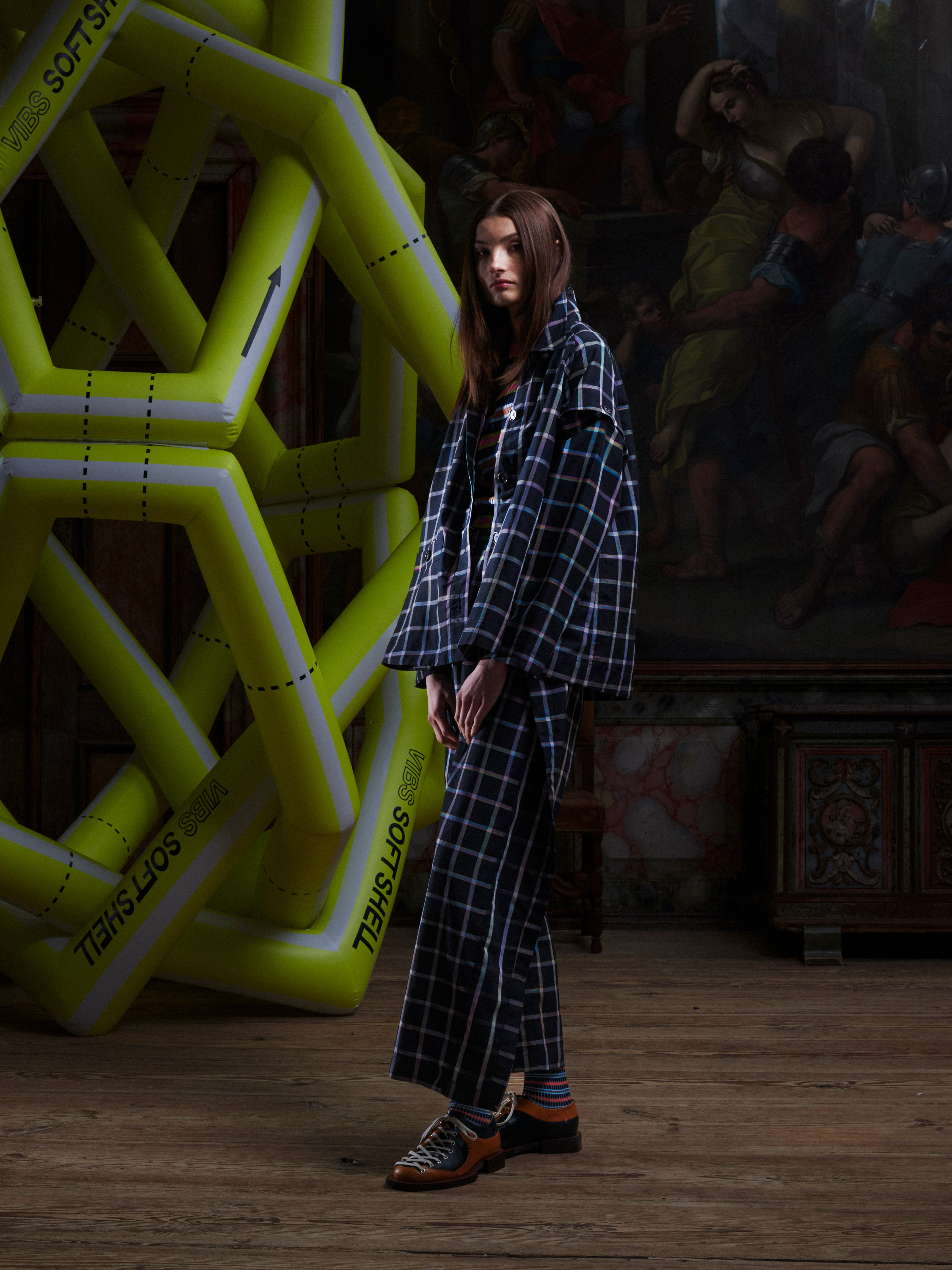 Side view of a female model wearing the Cover Coat in Black Checks from Henrik Vibskov Spring/Summer 2026 Studio Collection, highlighting the detachable sleeves, side silhouette, and straight hem.