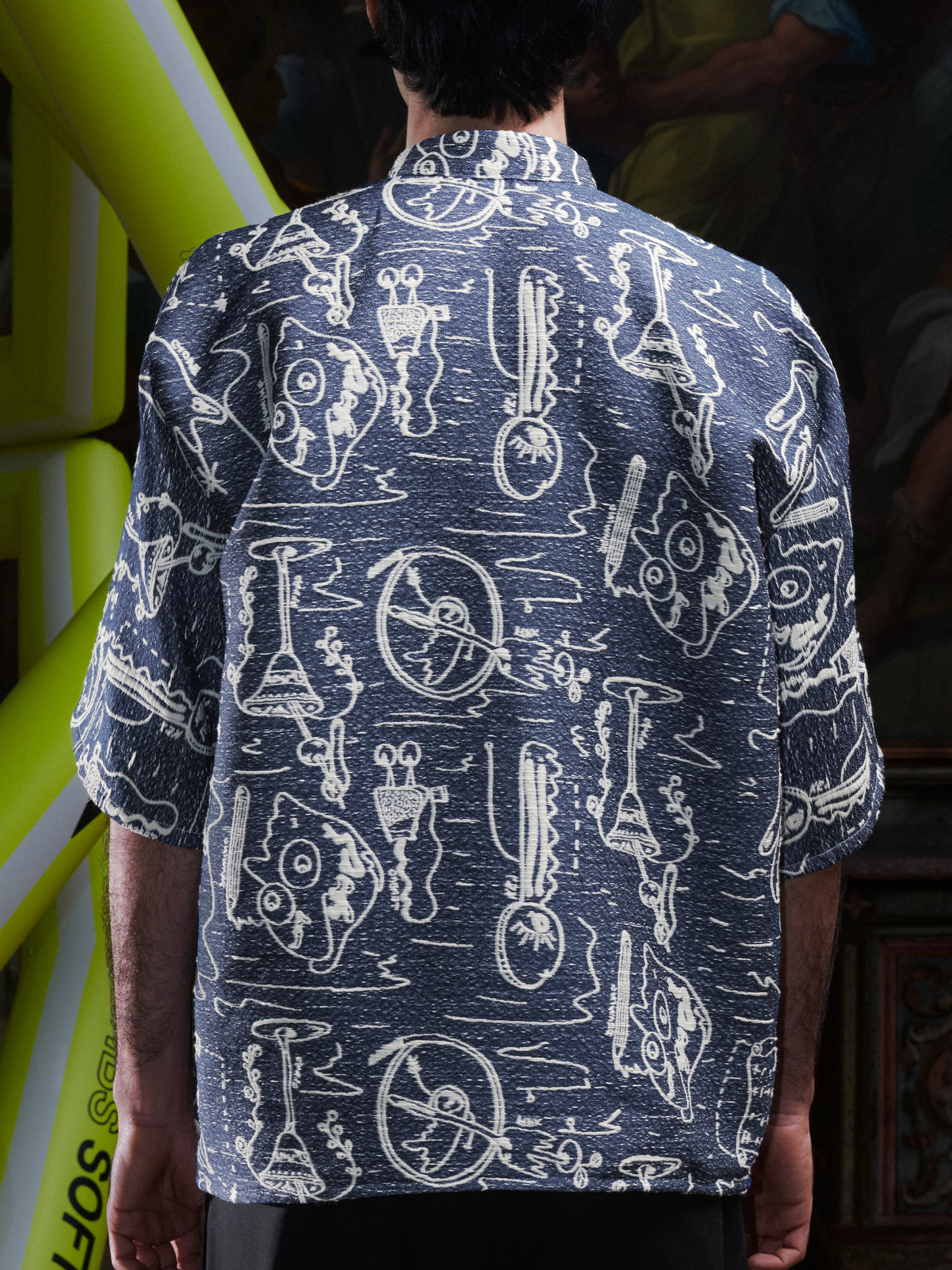 Close-up side view of the male model in the Dart Polo Shirt, showing the oversized sleeve shape and doodle print. Model is 181cm and wears size M.