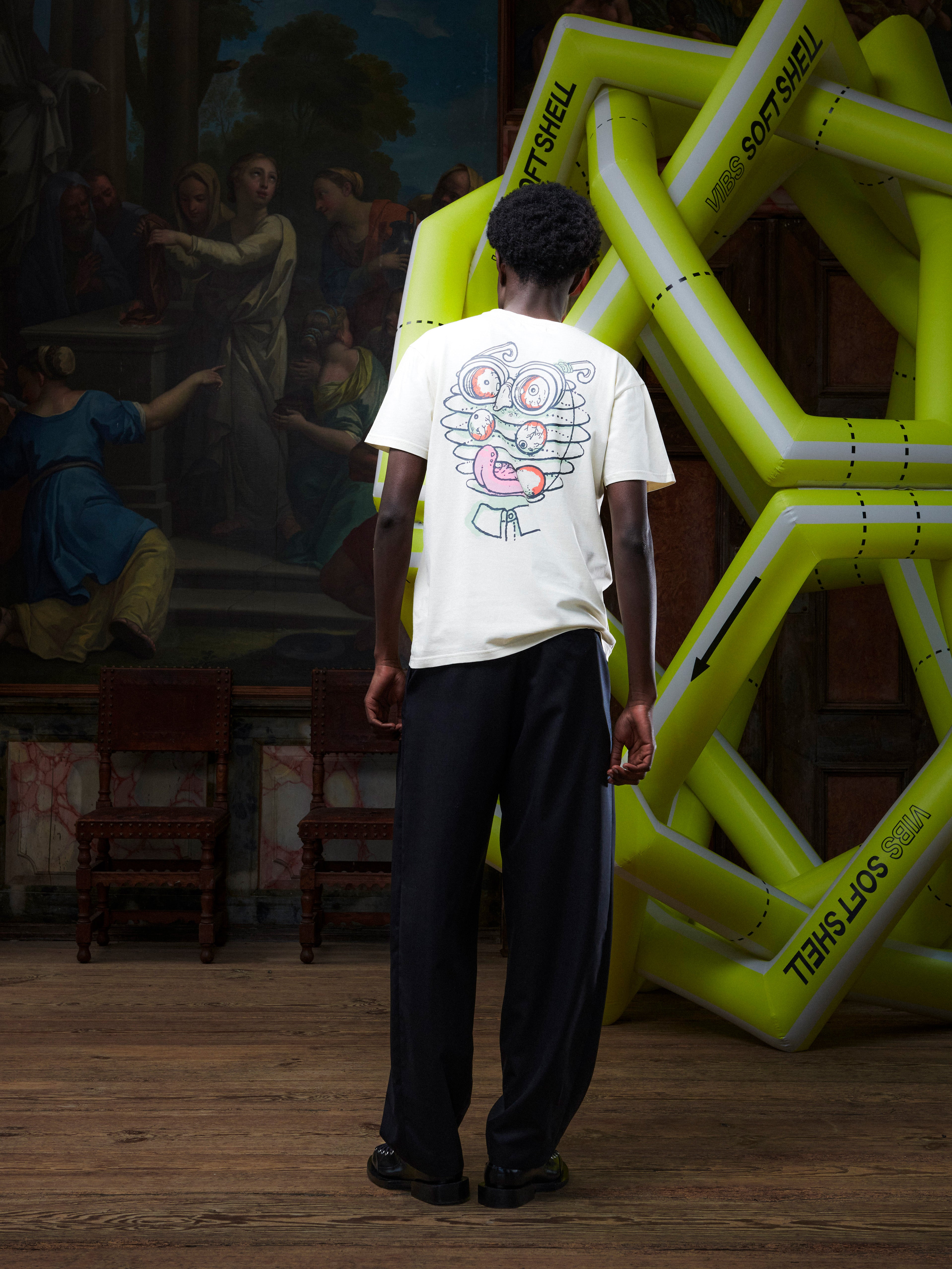 Model wearing the Henrik Vibskov Eyeballin T in Bone White, back view, showing the plain off-white back and straight hem.