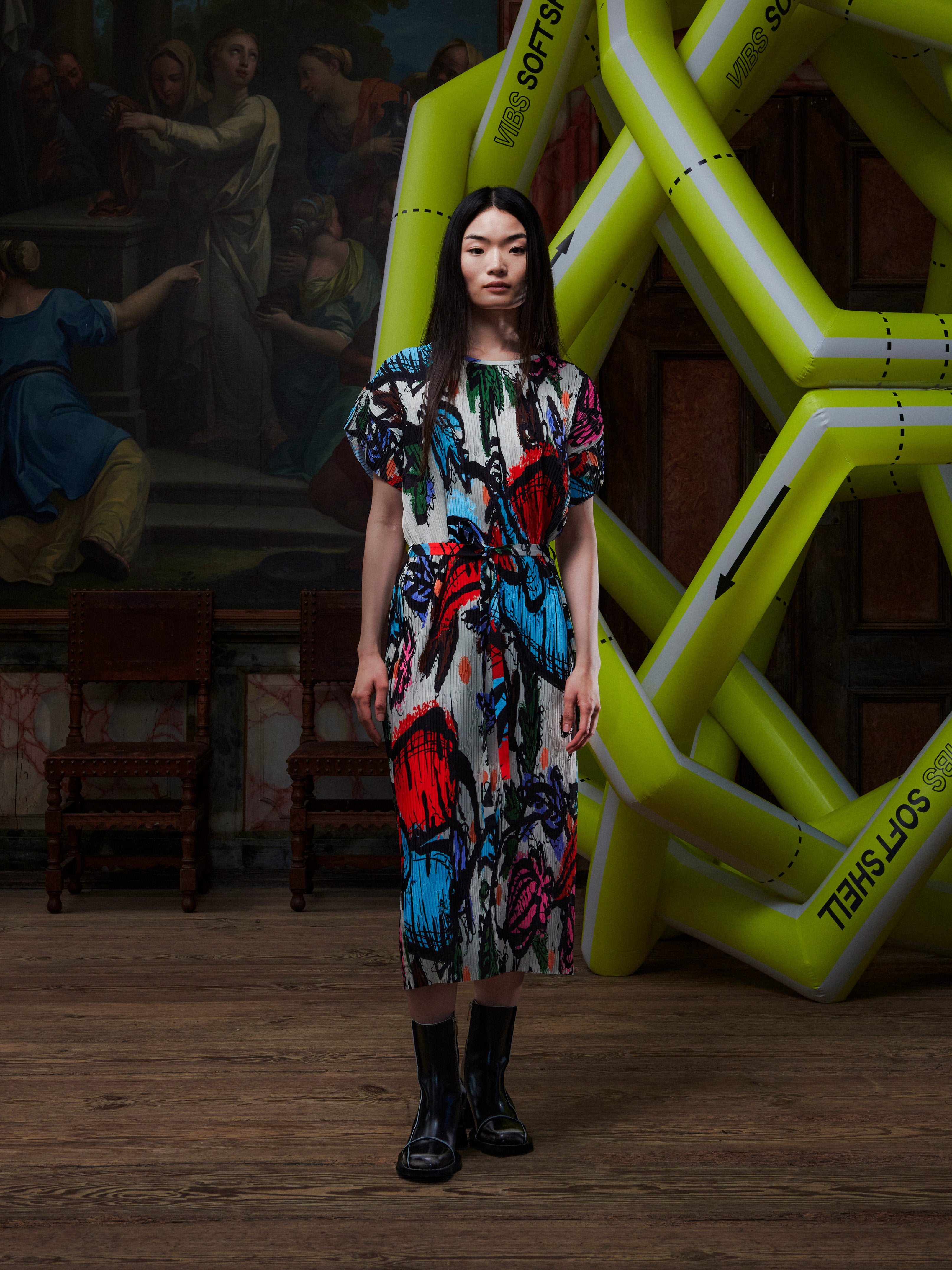 Model wearing the Henrik Vibskov New Pina Plissé Dress in Carrots, front view. The model is 167 cm and wears size S, showing the round neck, short sleeves, waist tie, and pleated multicolour print.