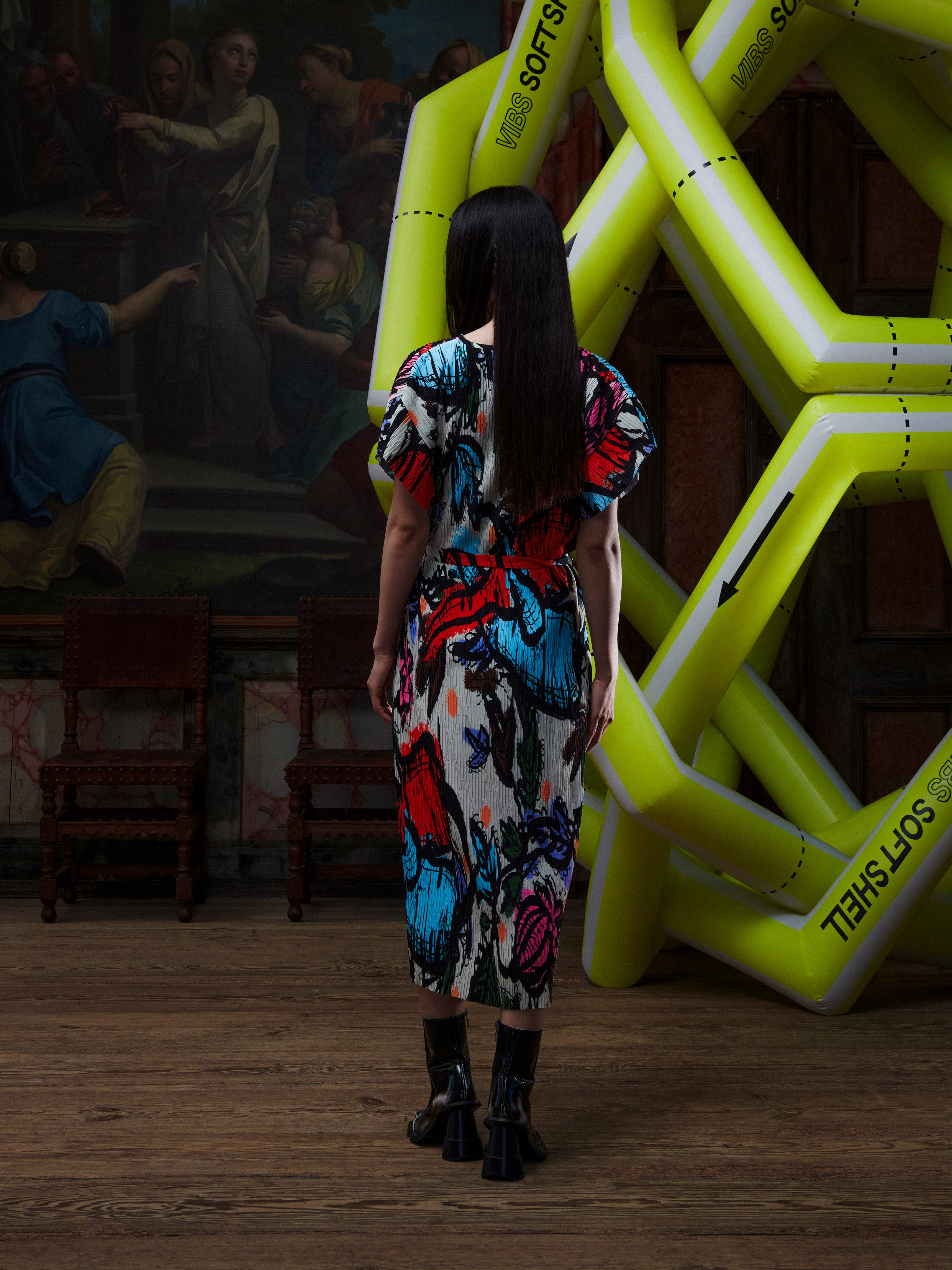 Model wearing the Henrik Vibskov New Pina Plissé Dress in Carrots, back view, showing the full multicolour illustration and pleated construction.