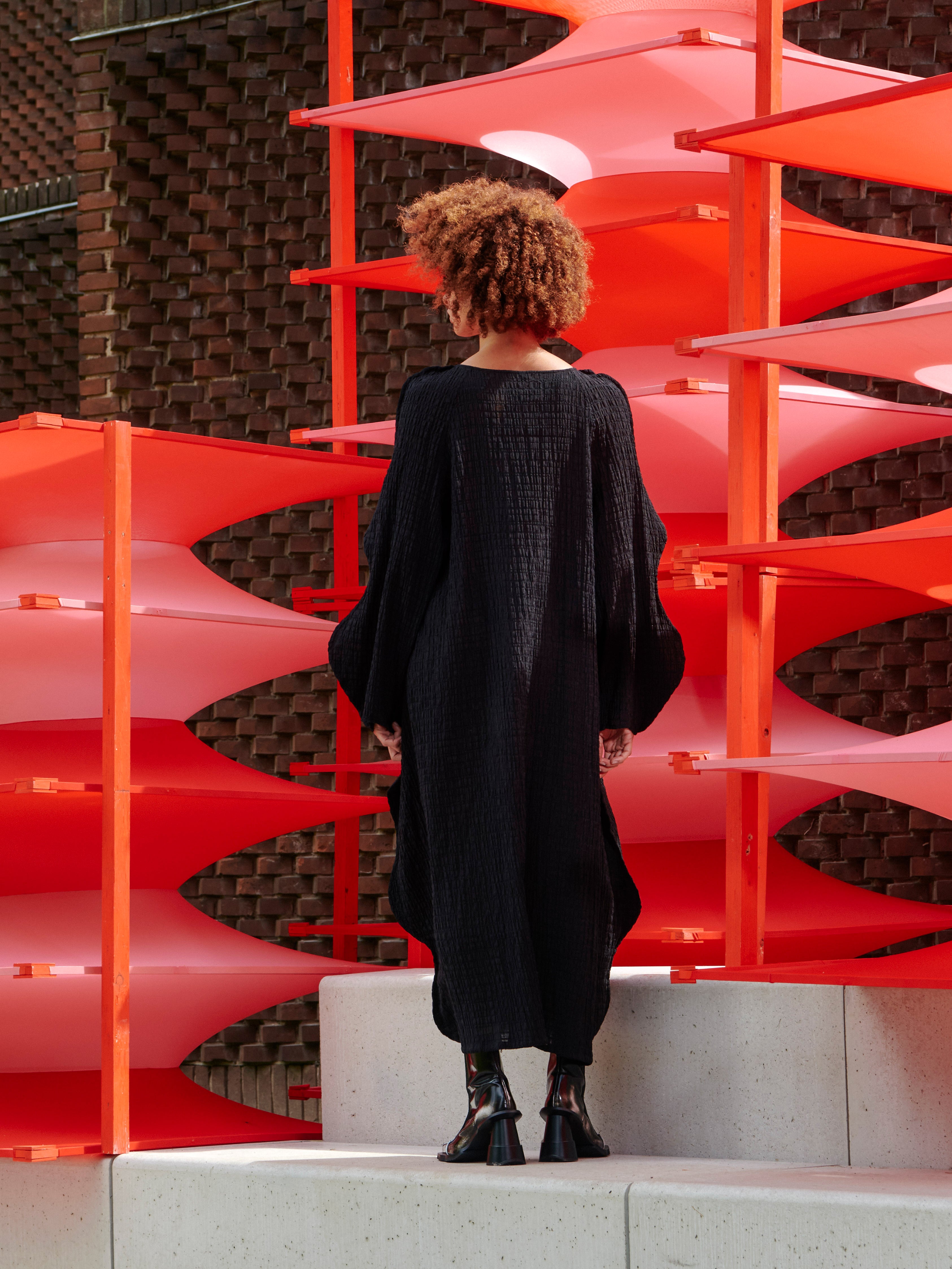 Model wearing the Octo Dress in Black black checkered textured dress with curved long sleeves and loose fit, back view – Henrik Vibskov Spring/Summer 2026 Key Collection