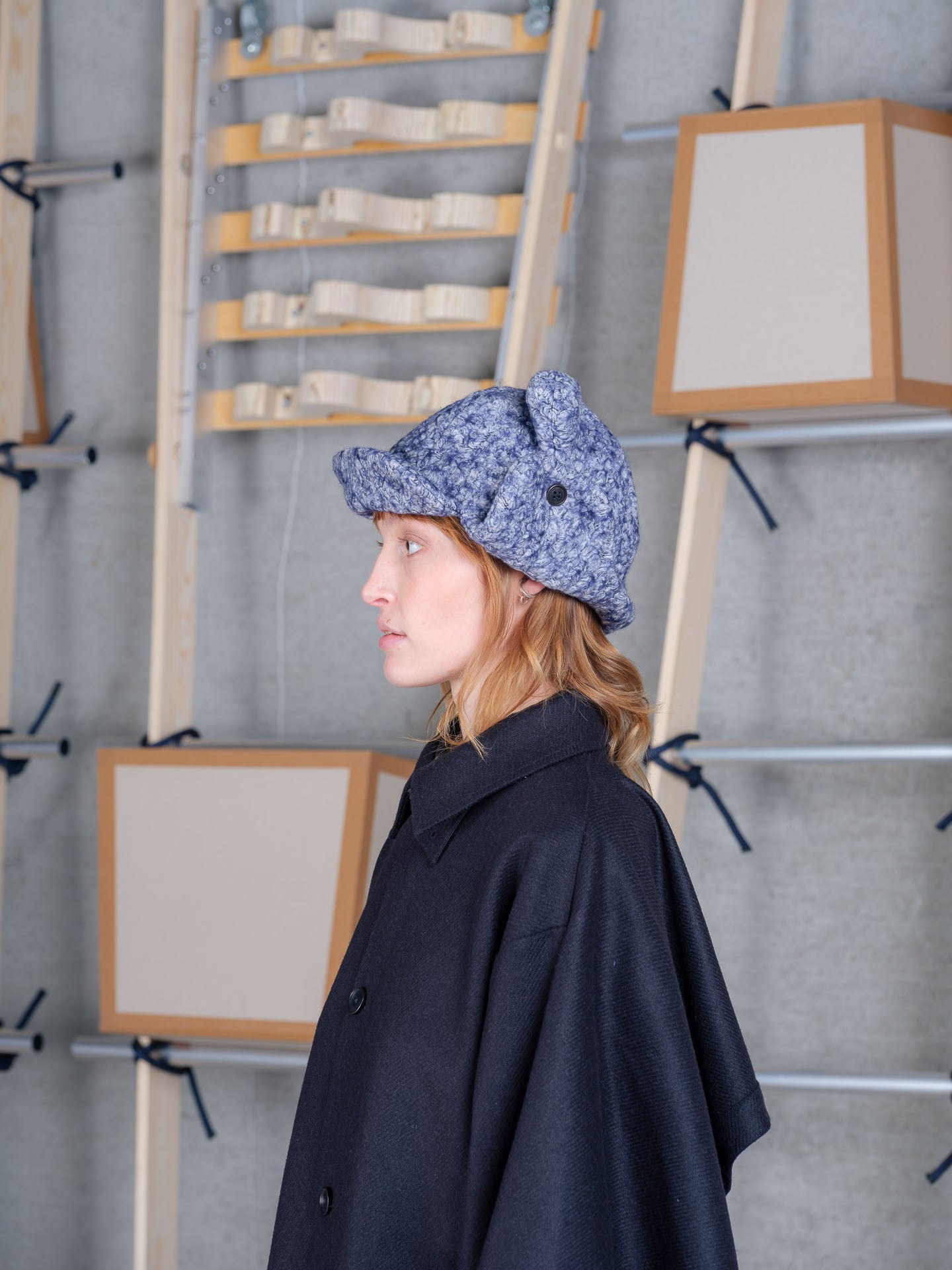 Side view of female model wearing Henrik Vibskov Pilot Frog Hat in blue pebbles showing folded side flaps, rounded panels and textured cotton finish