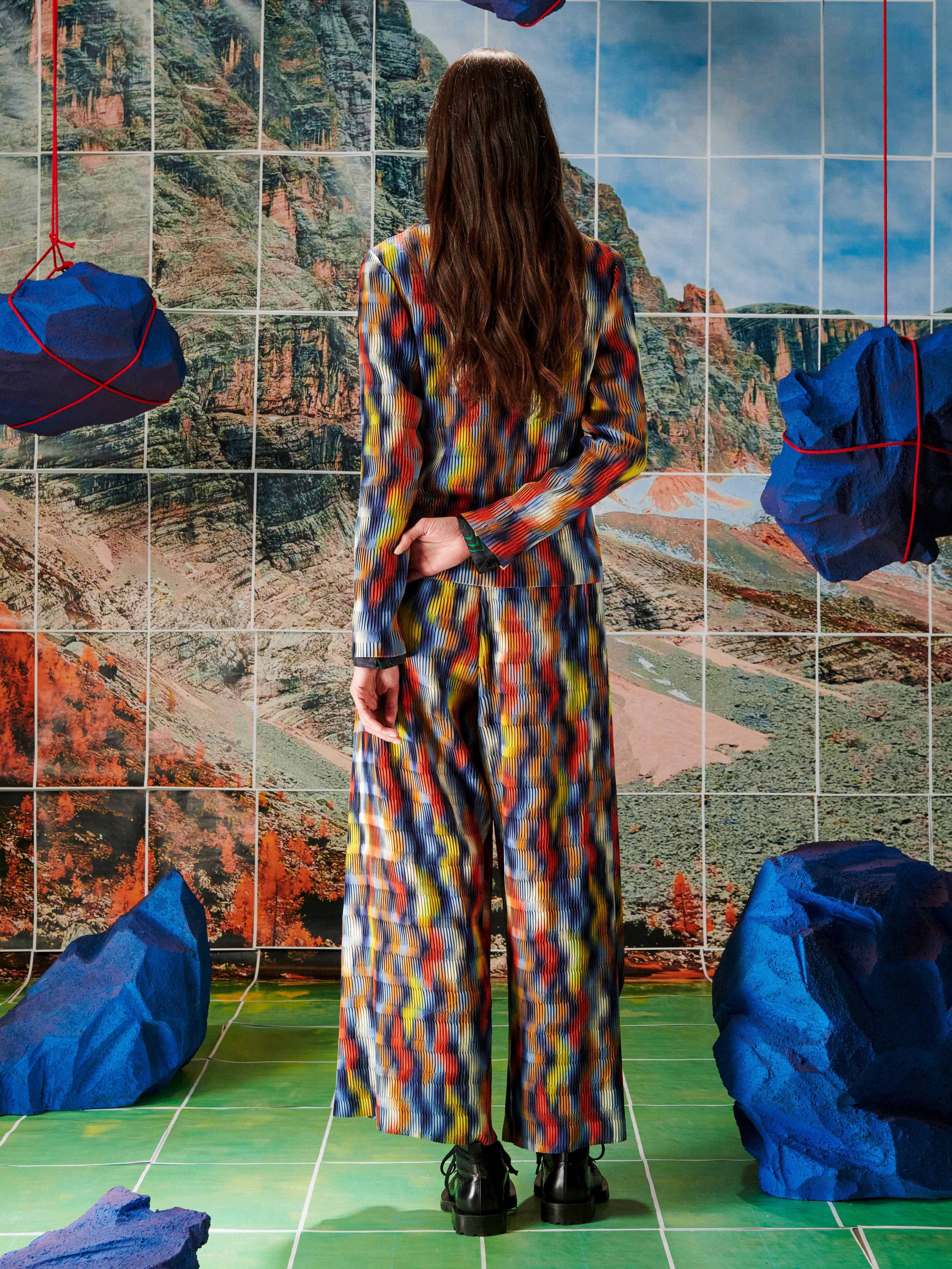Person wearing a colorful suit standing in front of a tiled wall with abstract art.