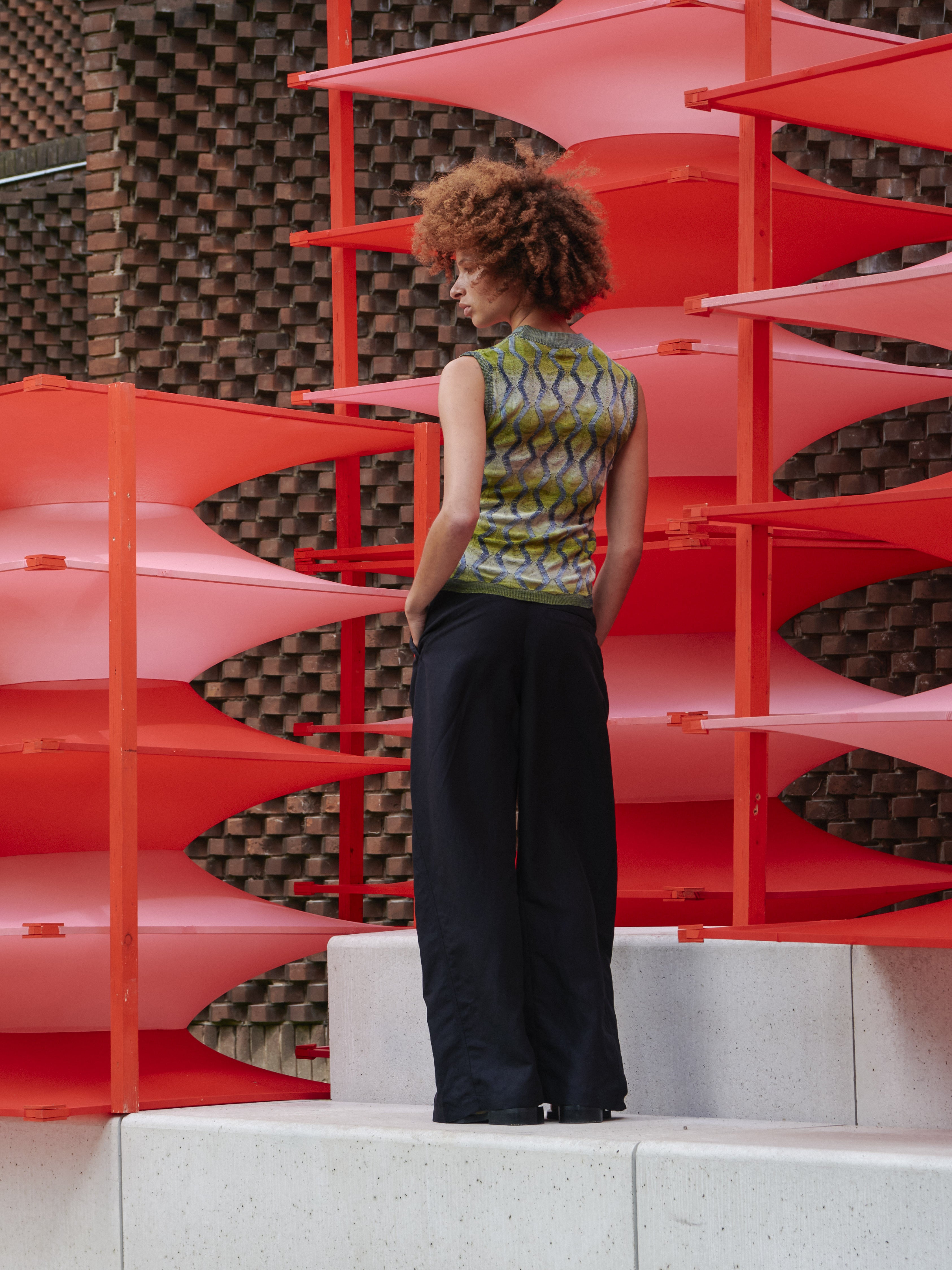 Back view of model wearing Henrik Vibskov Resonance Top in Multi Flame, highlighting sleeveless fit, ribbed hems, and vibrant green with silver patterned viscose fabric from SS26 collection.