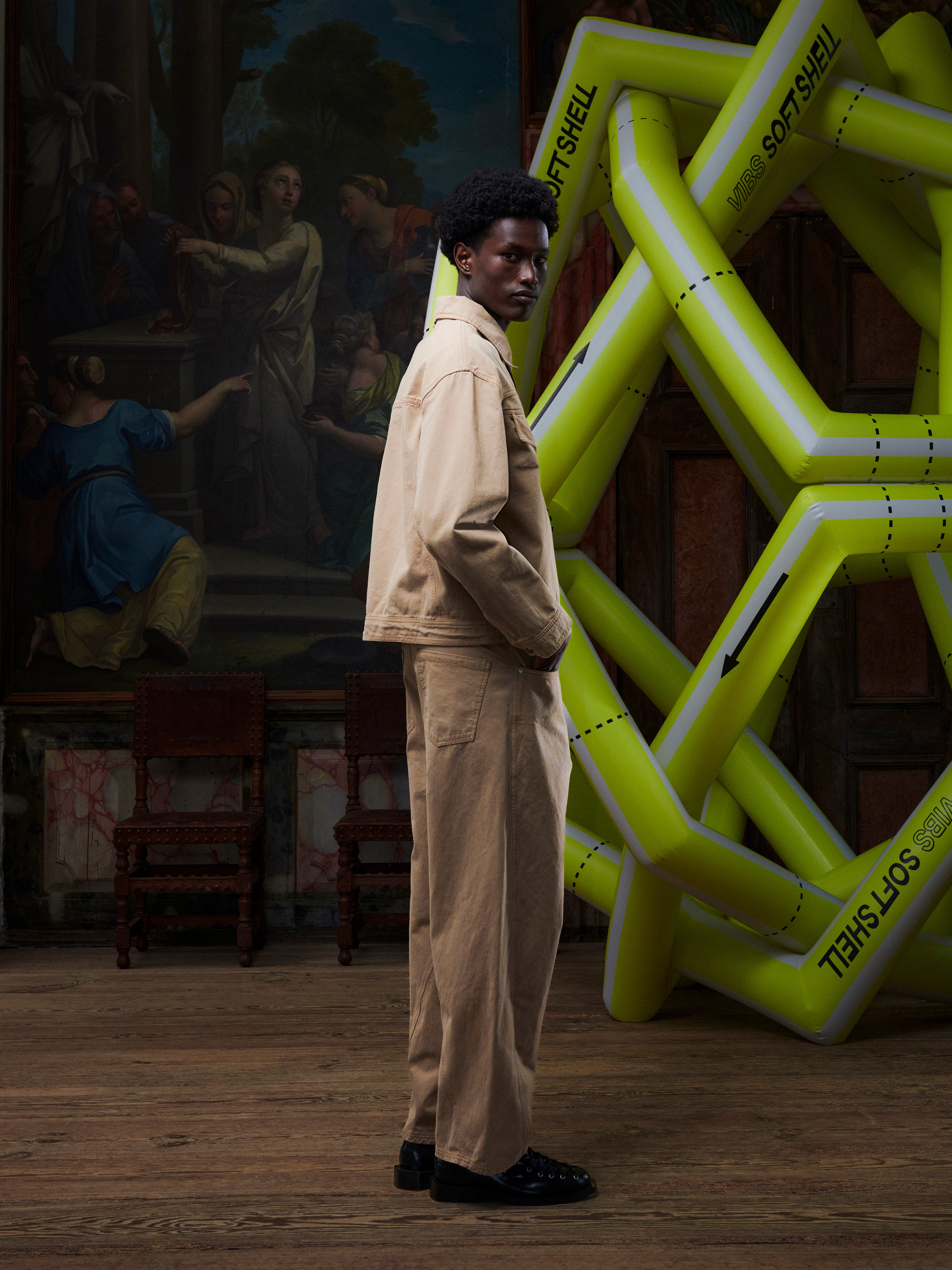 Side profile of someone wearing the Dark beige denim jacket from Henrik Vibskov in front of an inflatable structure
