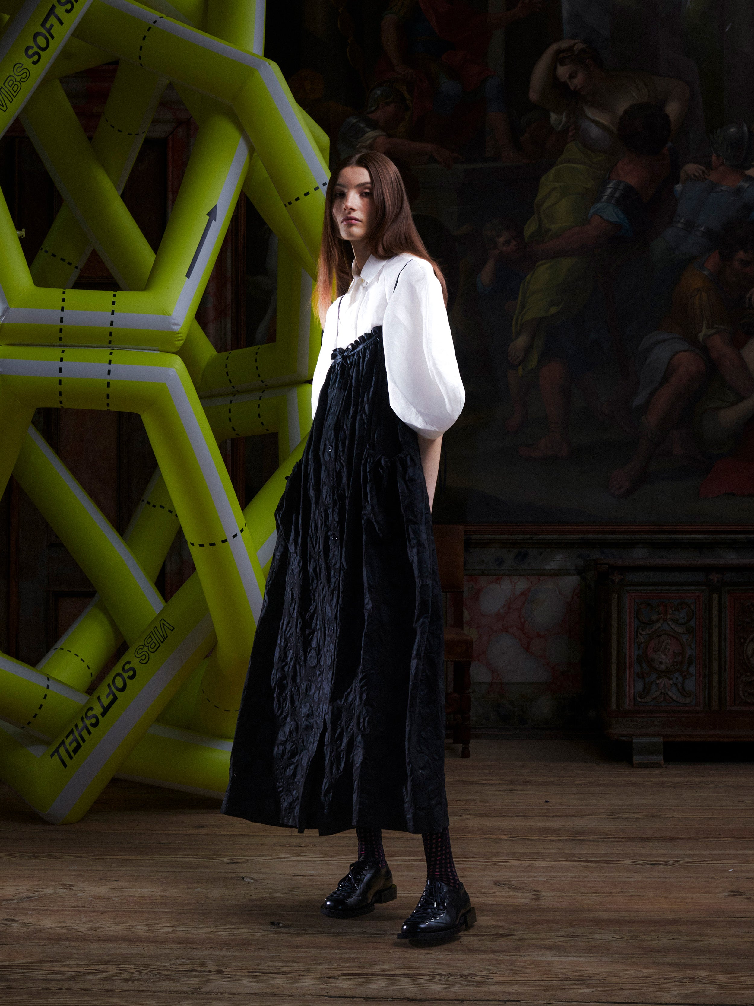Side profile of woman wearing the black-on-black pattern, sleeveless dress on top of a white blouse from Henrik Vibskov.