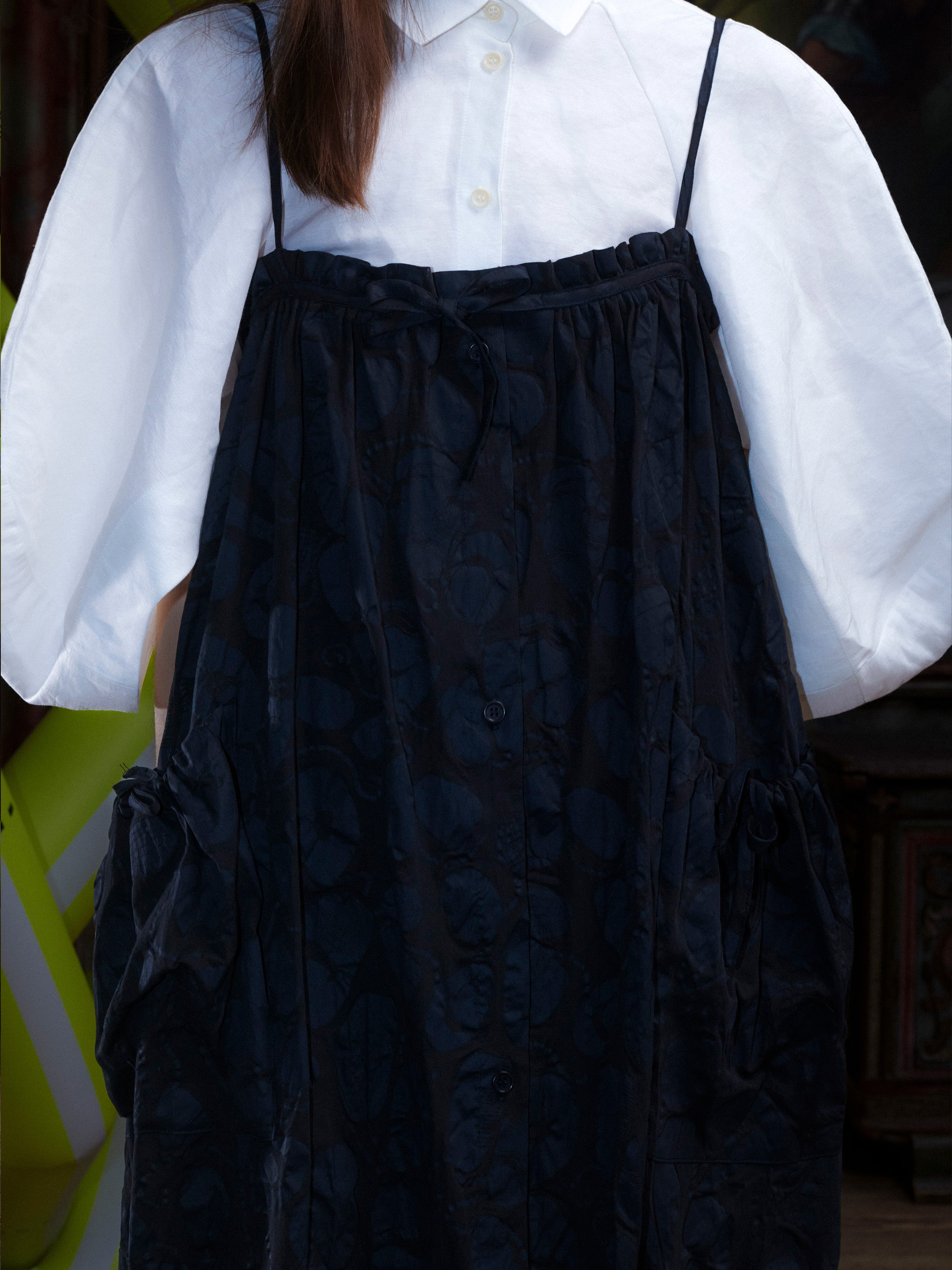 Close-up of a woman wearing the black-on-black pattern, sleeveless dress on top of a white blouse from Henrik Vibskov.
