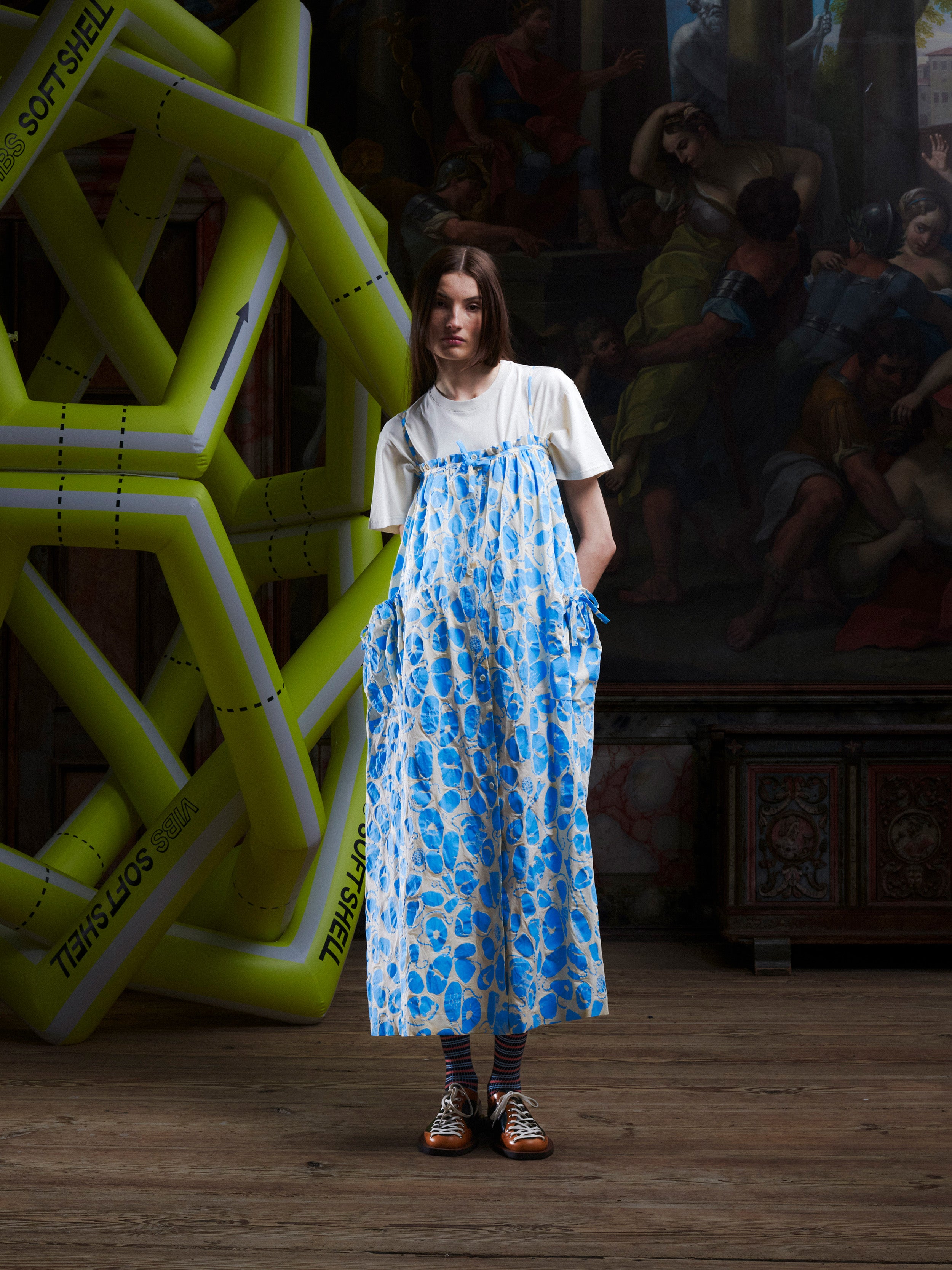 Woman wearing the off-white and light blue pattern, sleeveless dress on top of a white t-shirt from Henrik Vibskov.