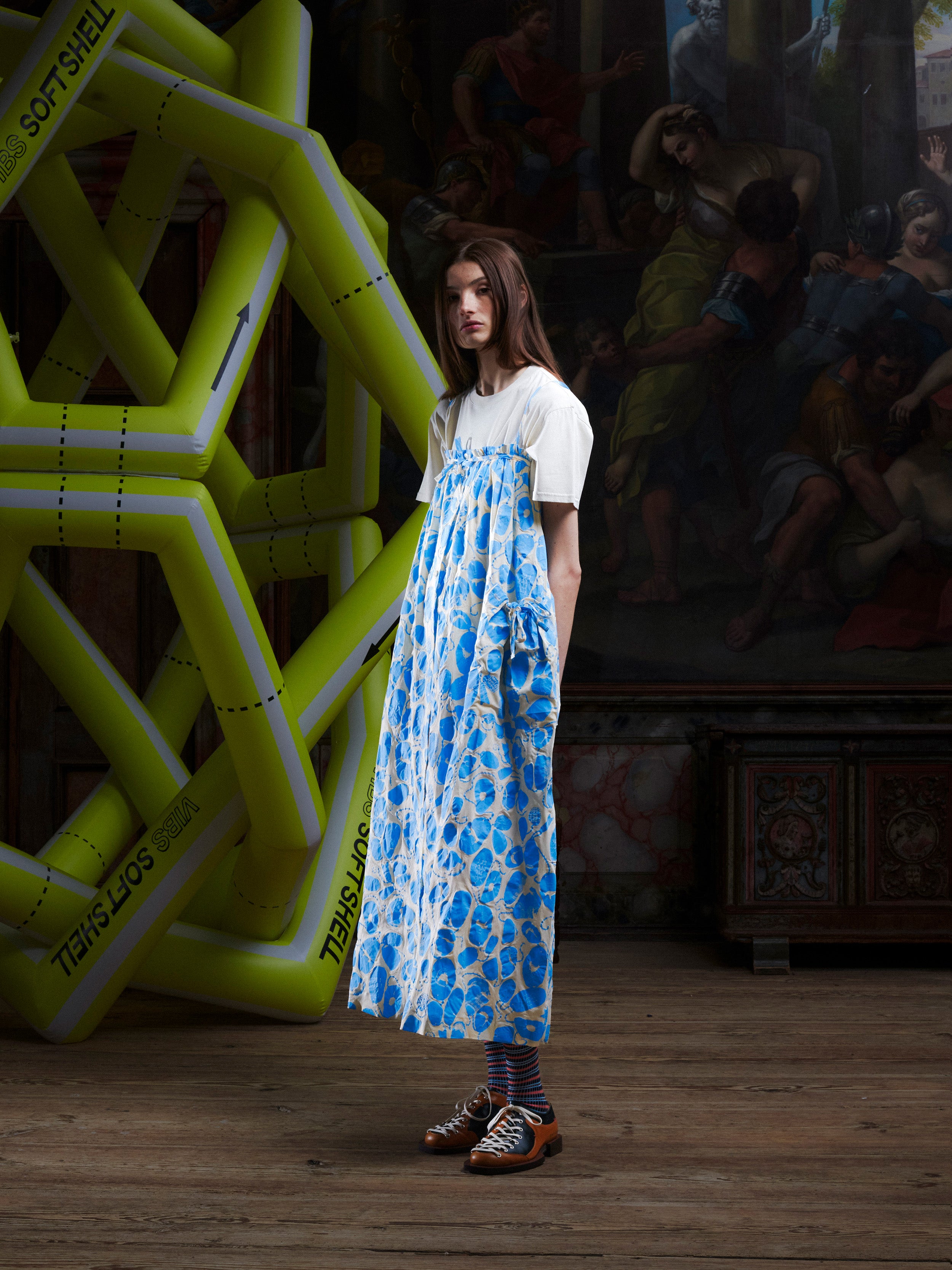 Side profile of a woman wearing the off-white and light blue pattern, sleeveless dress on top of a white t-shirt from Henrik Vibskov.