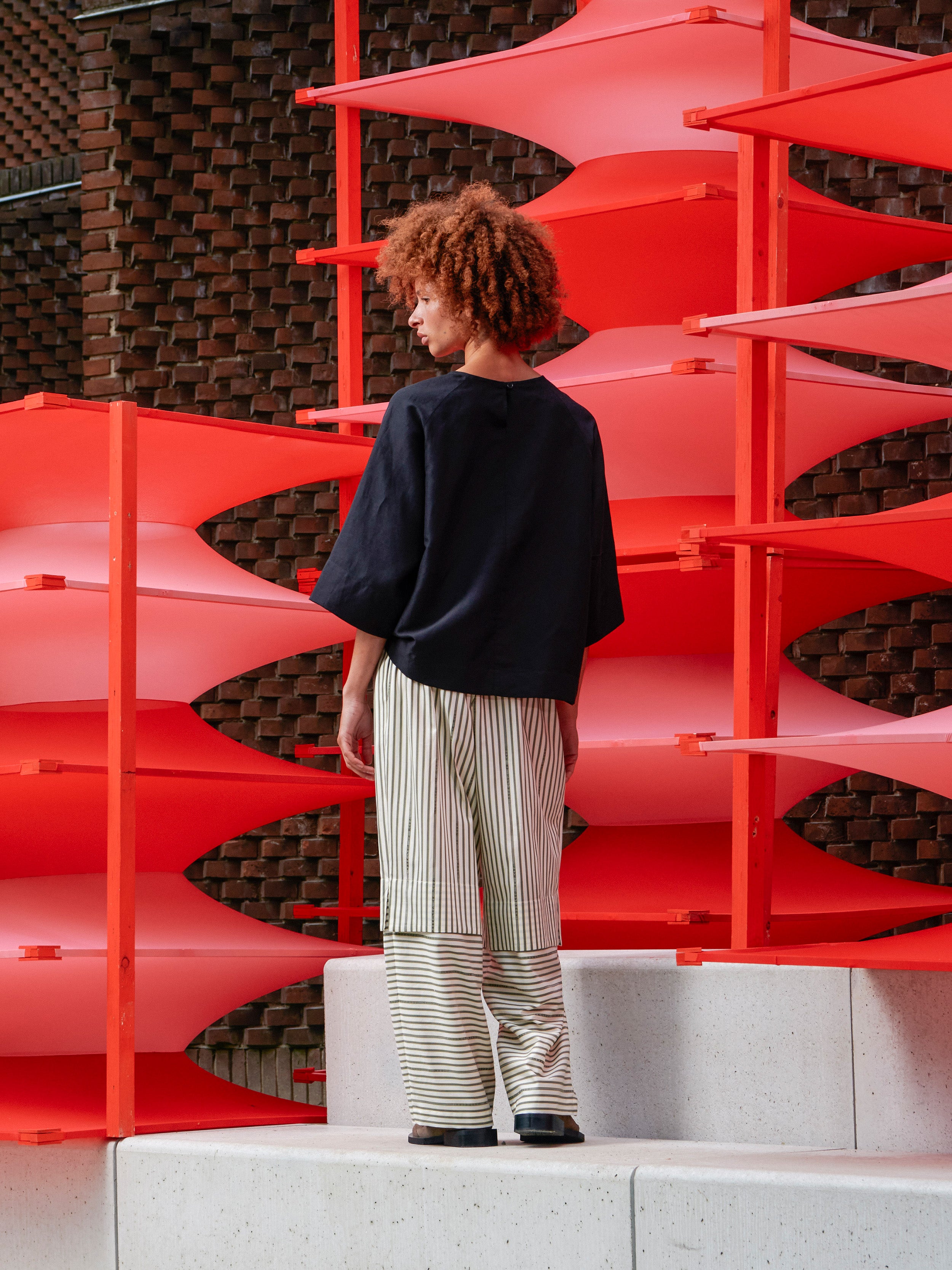 Back view of a model wearing the Shants Pants, showing the layered design, wide-leg silhouette, and striped text pattern.