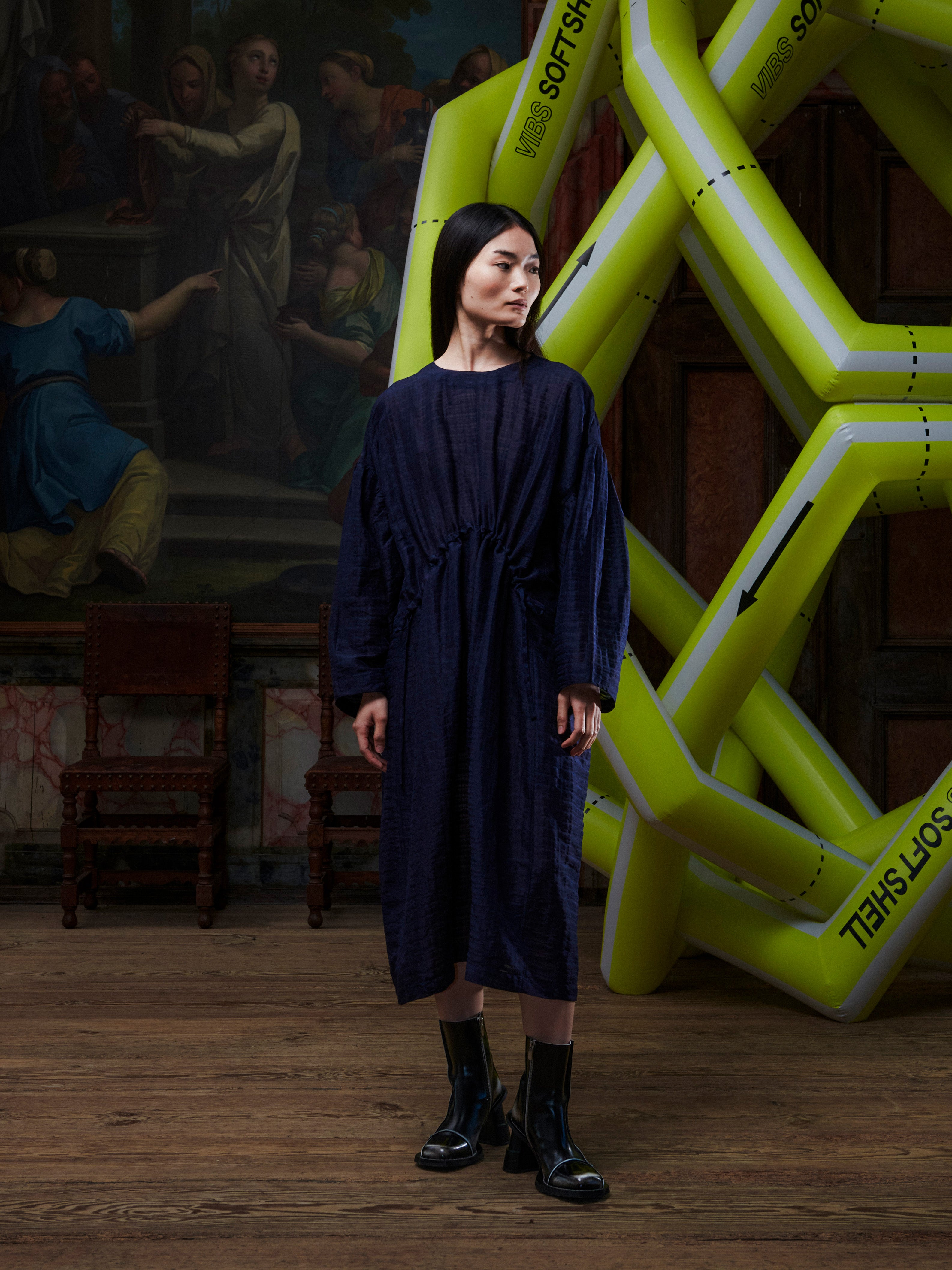 Woman wearing the navy long sleeve dress from Henrik Vibskov in front of a yellow inflatable sculpture.