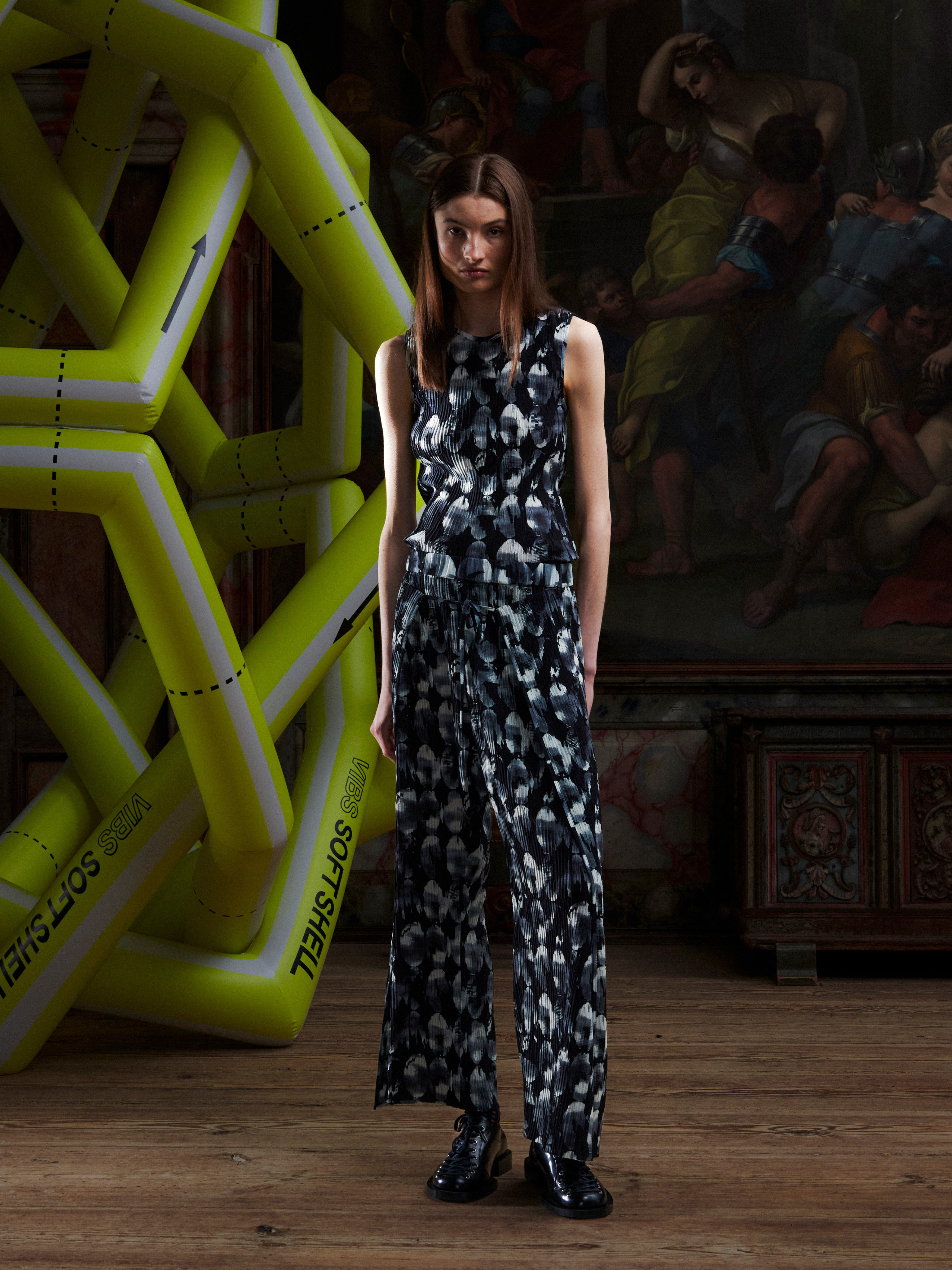 Woman in a black and white patterned top and pants standing in front of a large inflatable sculpture and artwork.