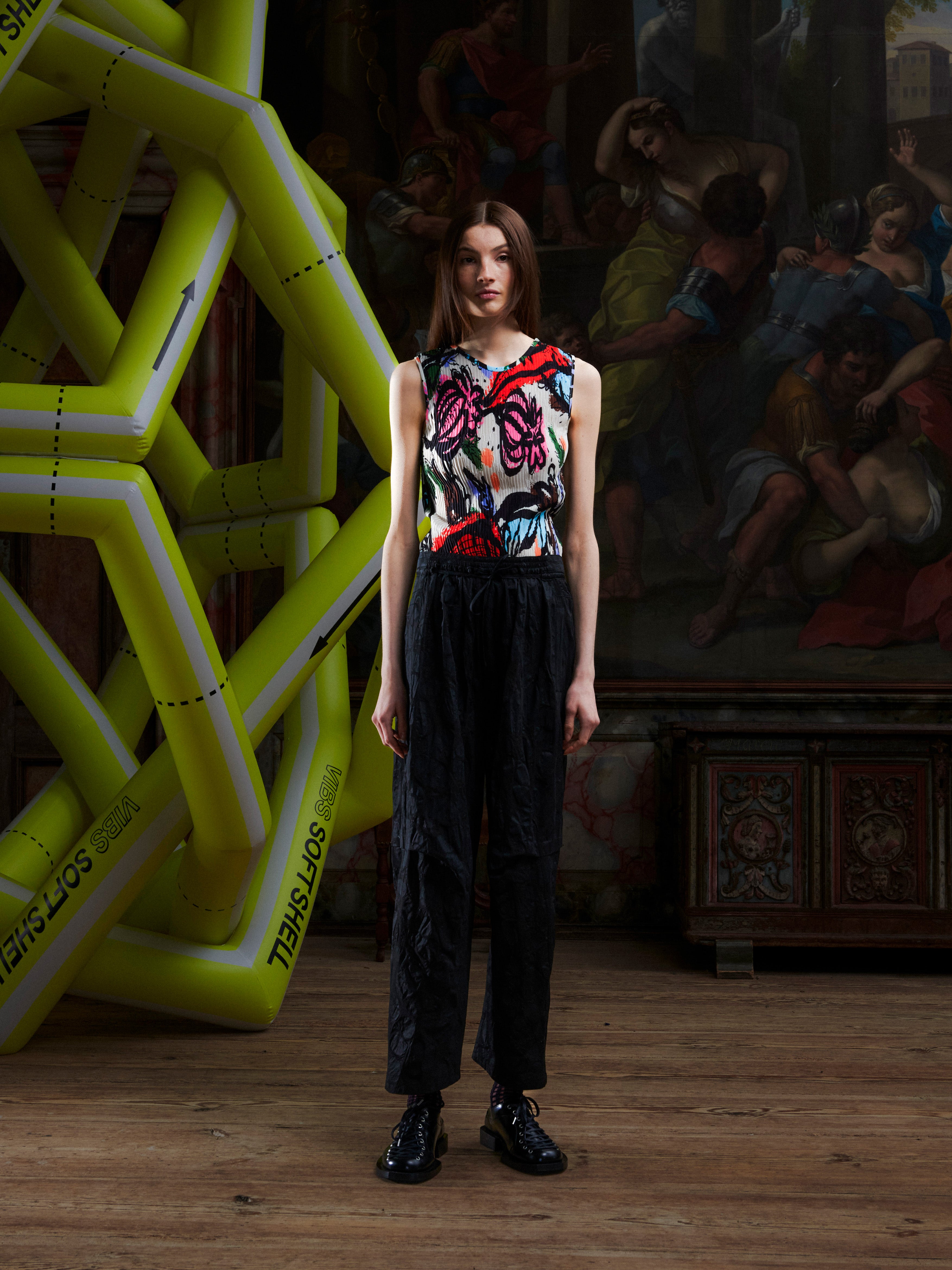 Woman in a colorful top and black pants standing in front of an artistic backdrop with a large inflatable sculpture.