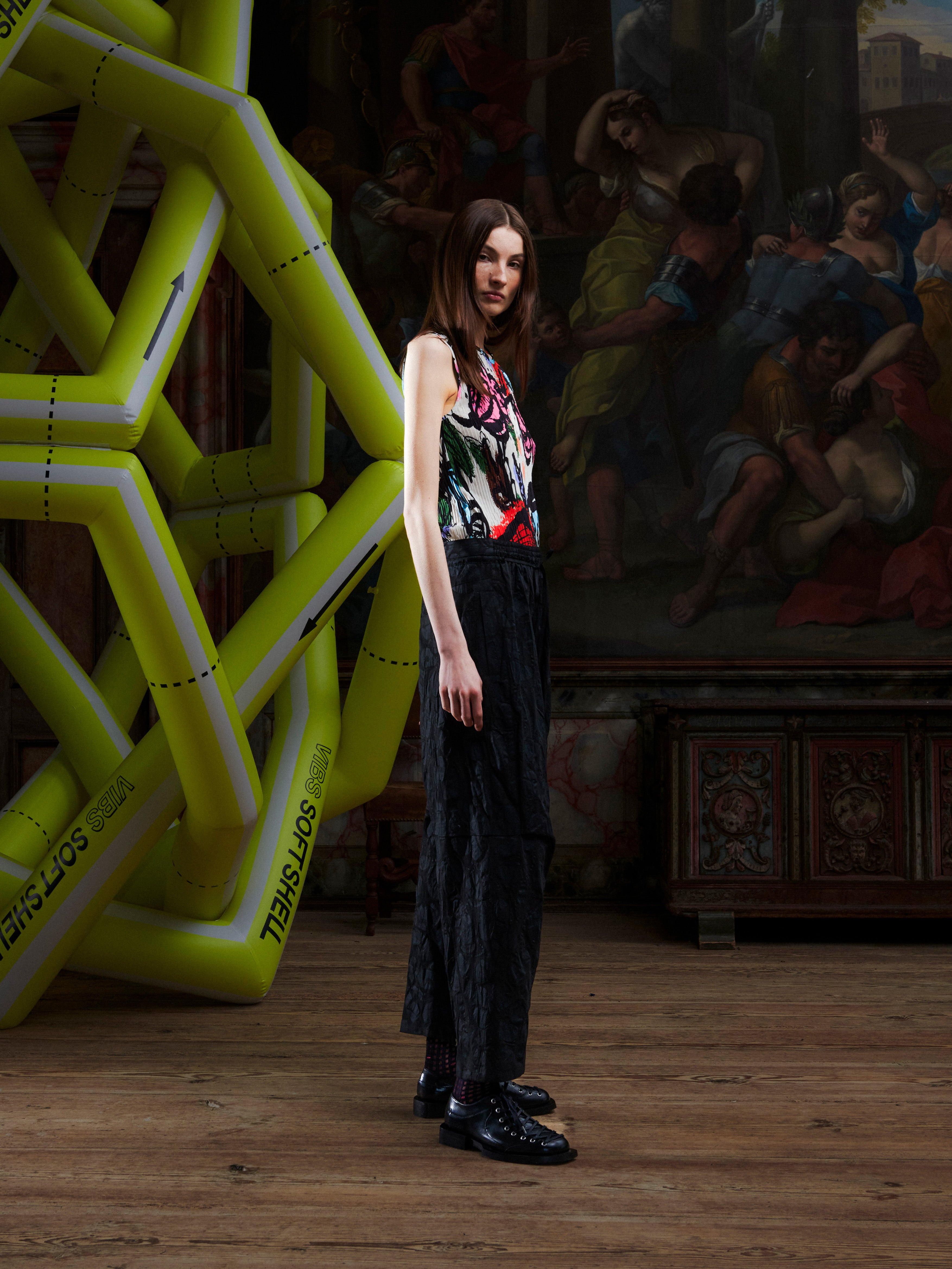 Side profile of woman in a colorful top and black pants standing in front of an artistic backdrop with a large inflatable sculpture.