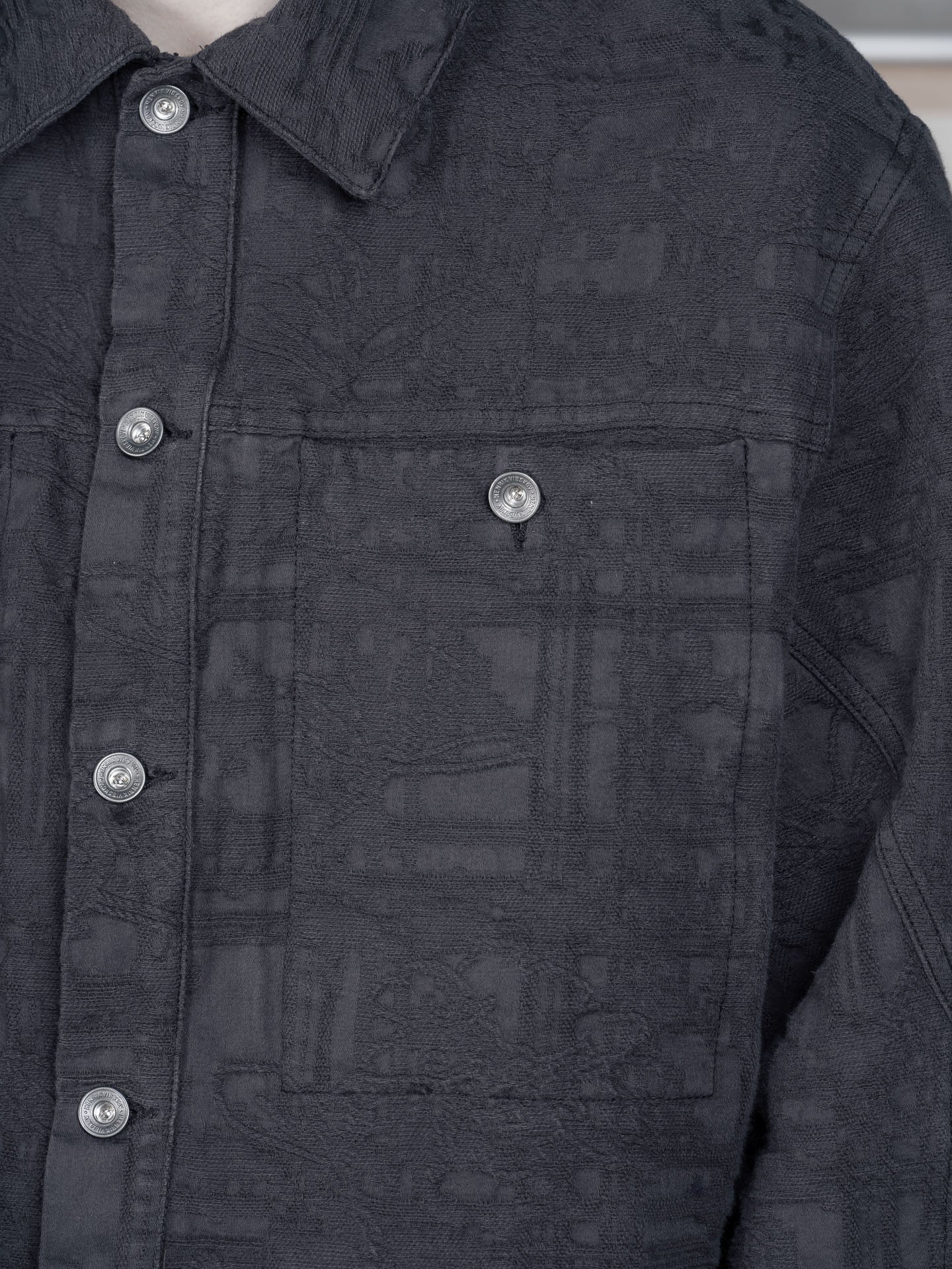 Henrik Vibskov Toadally Denim Jacket in Black, close-up of chest flap pocket, silver press-stud fastening, tonal jacquard texture, point collar