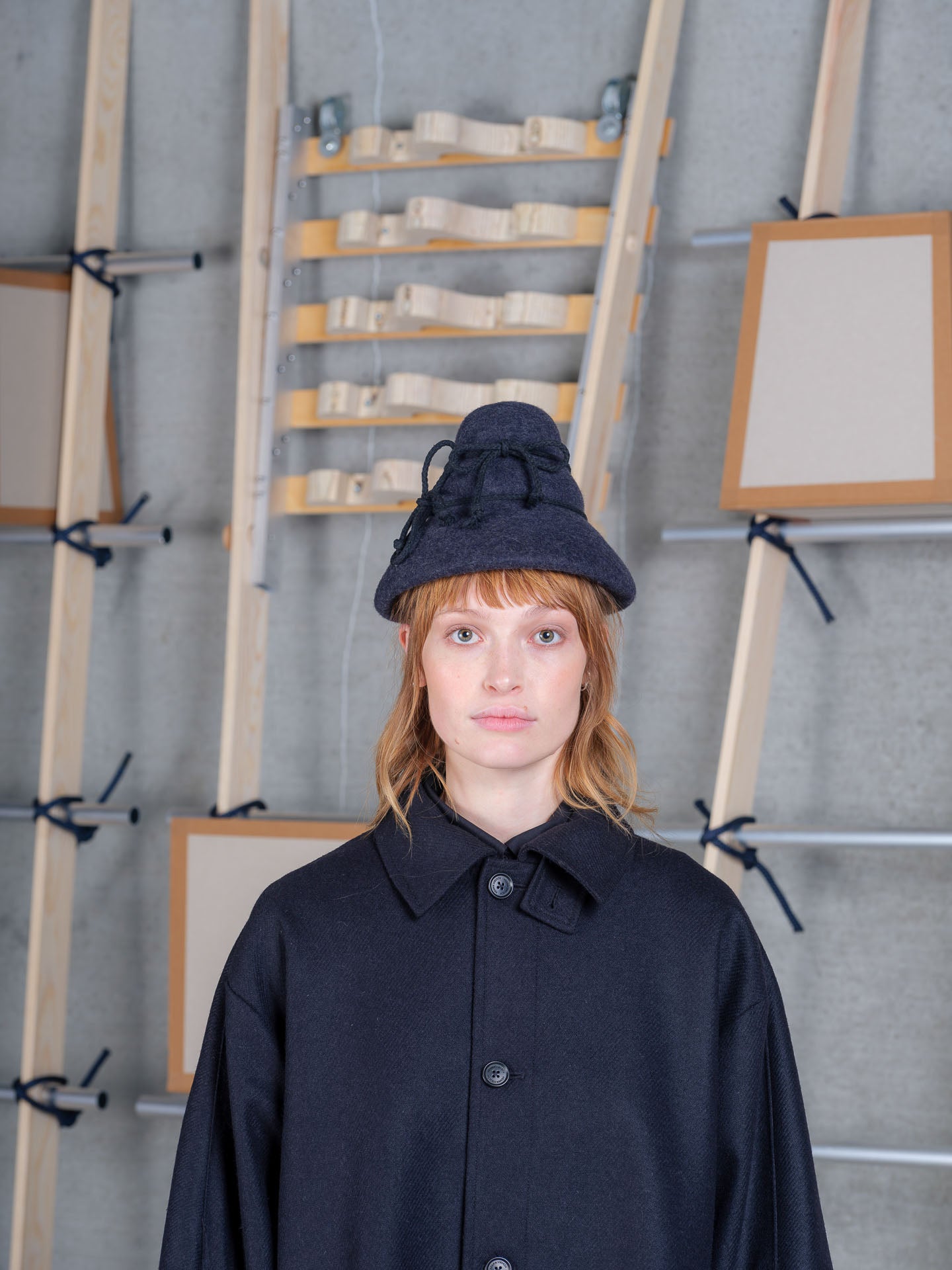Model wearing the Henrik Vibskov Tower Hat in charcoal with a navy wool coat, front view