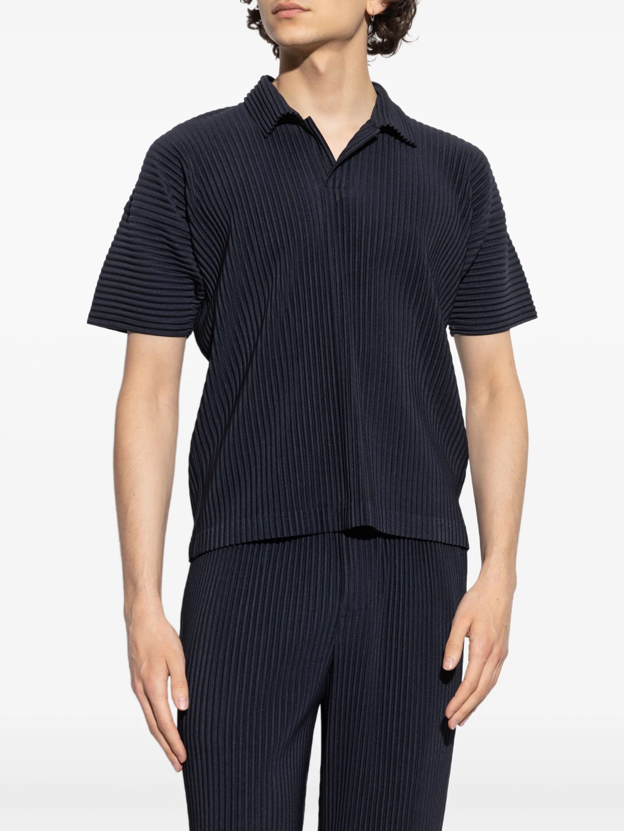 Person wearing a dark blue ribbed polo and pants on a white background