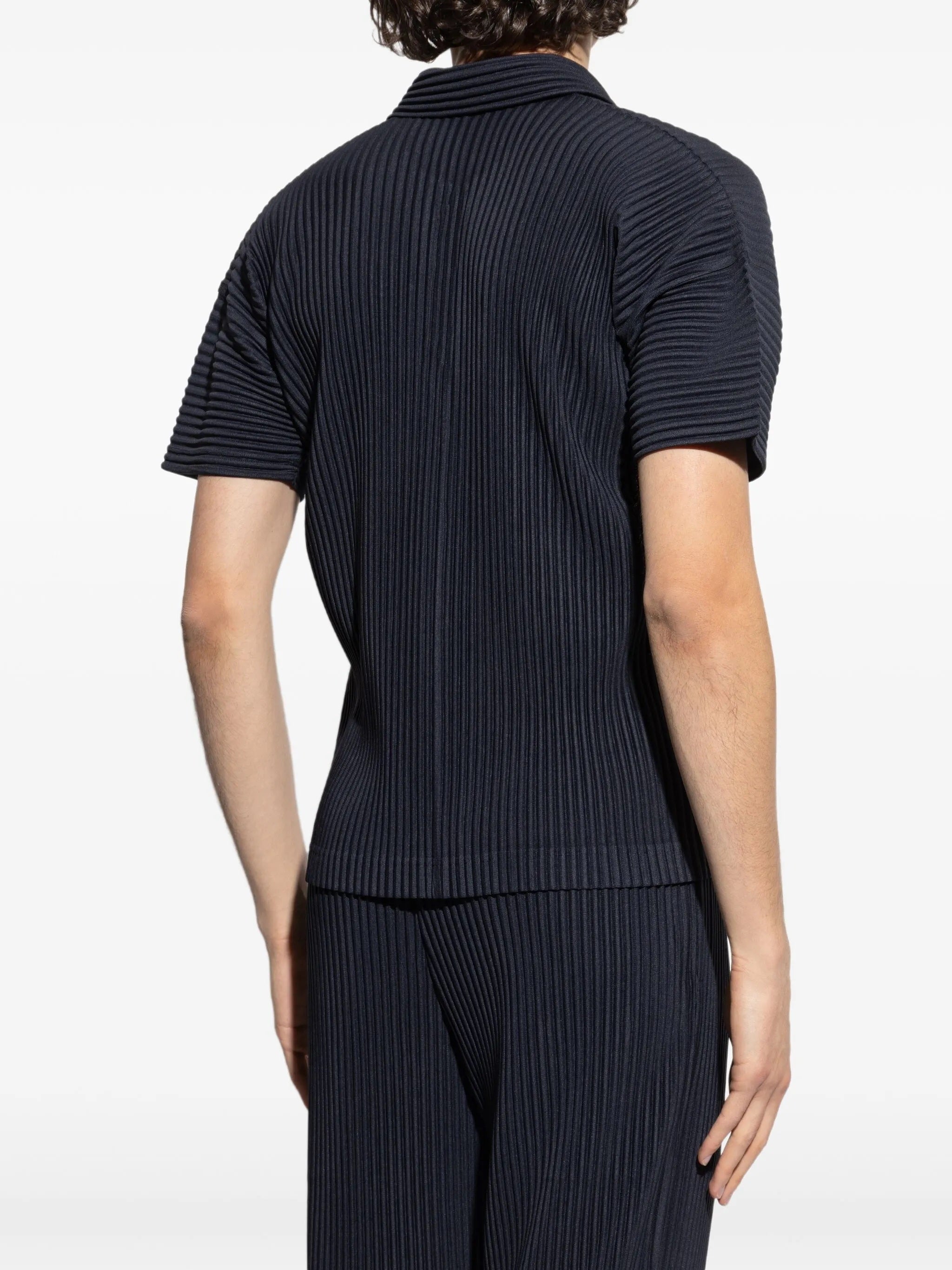 Person wearing a dark blue ribbed polo and pants on a white background