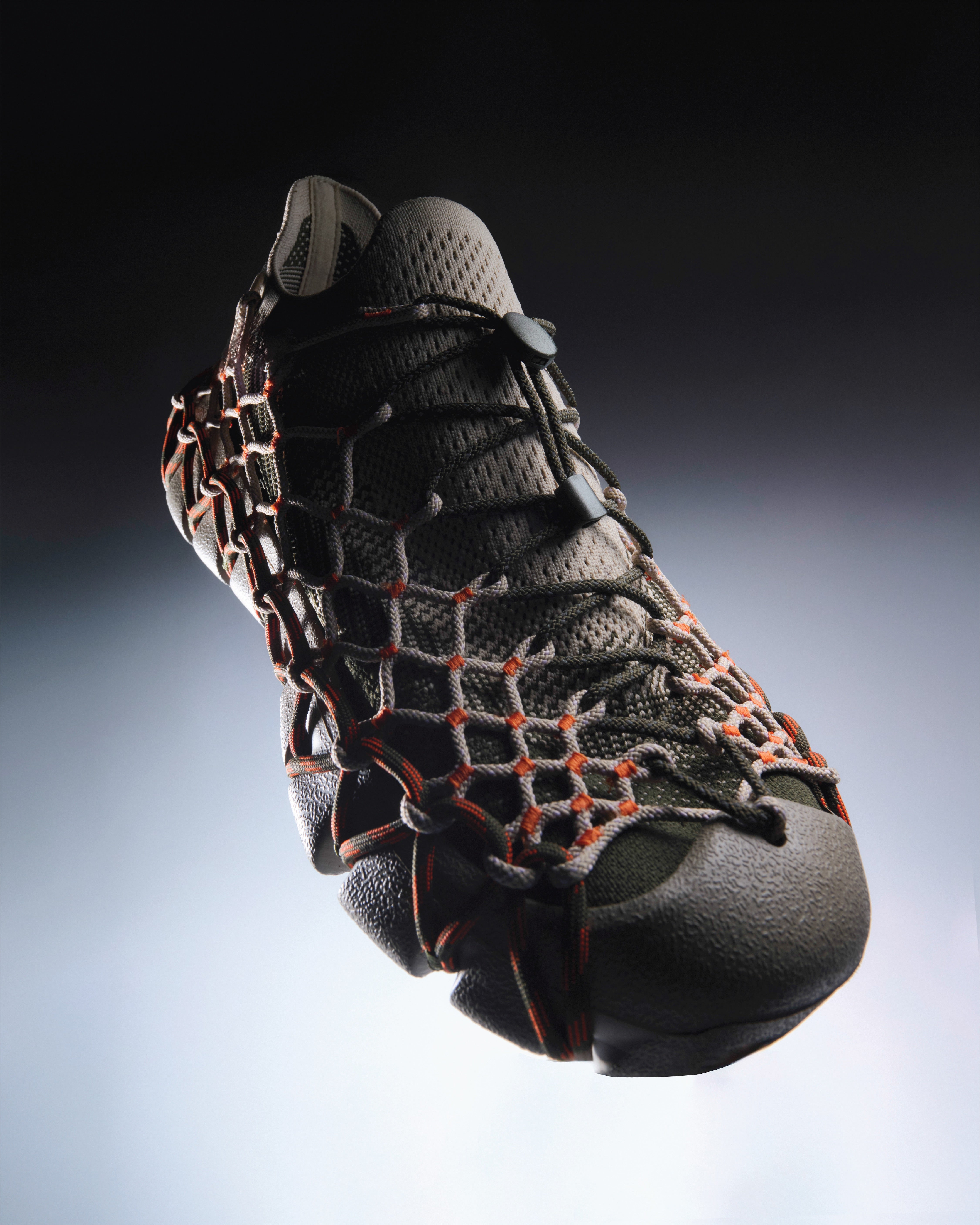 Henrik Vibskov x KEEN UNEEK 360 Sneakers in Brindle Scarlet Ibis a grey knit sneaker with an orange and grey rope net overlay, floating against a dark gradient background.