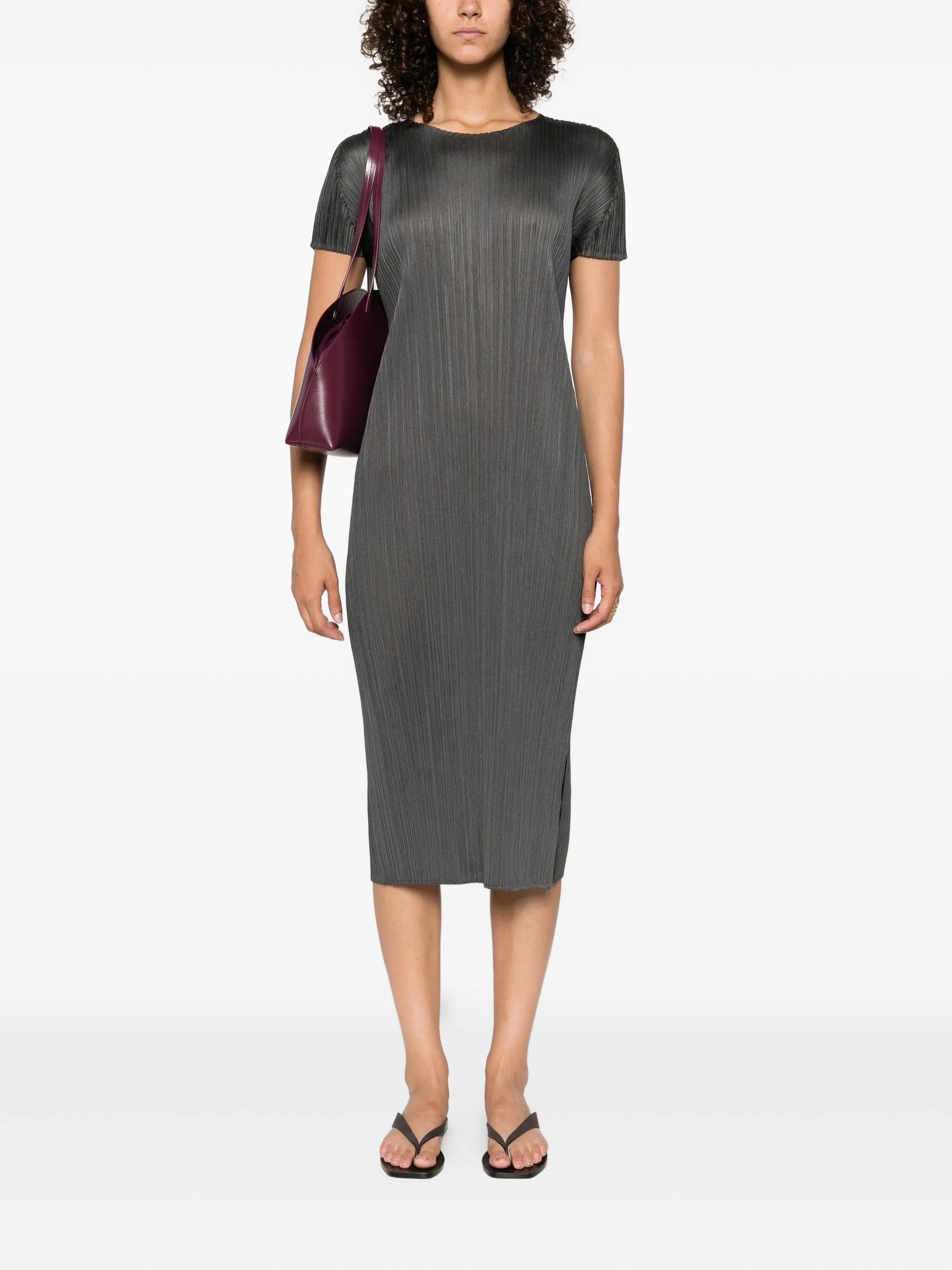 Woman wearing a gray pleated dress with a maroon handbag on a white background