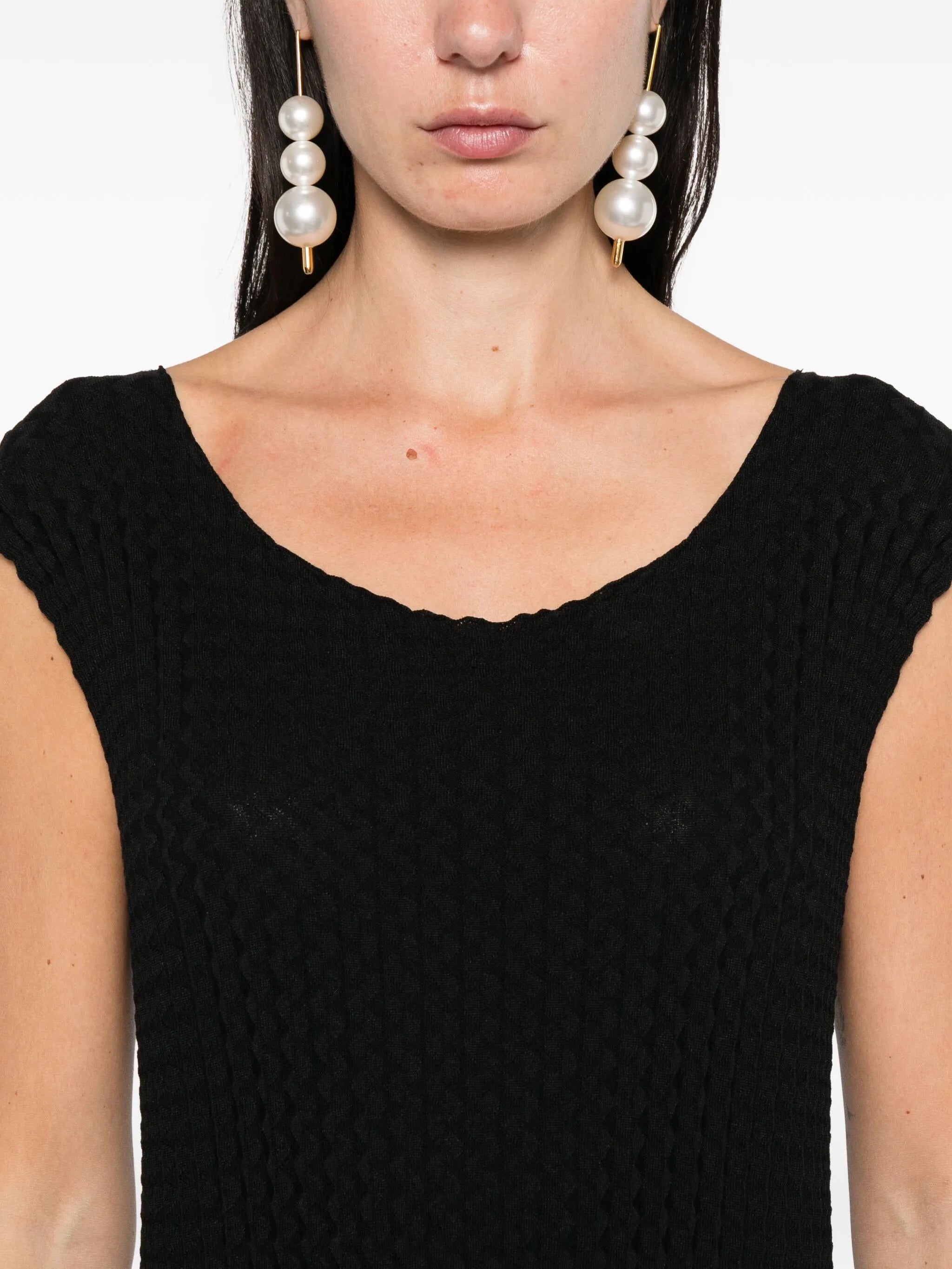 Close-up of a person wearing a black Issey Miyake dress with a plain background