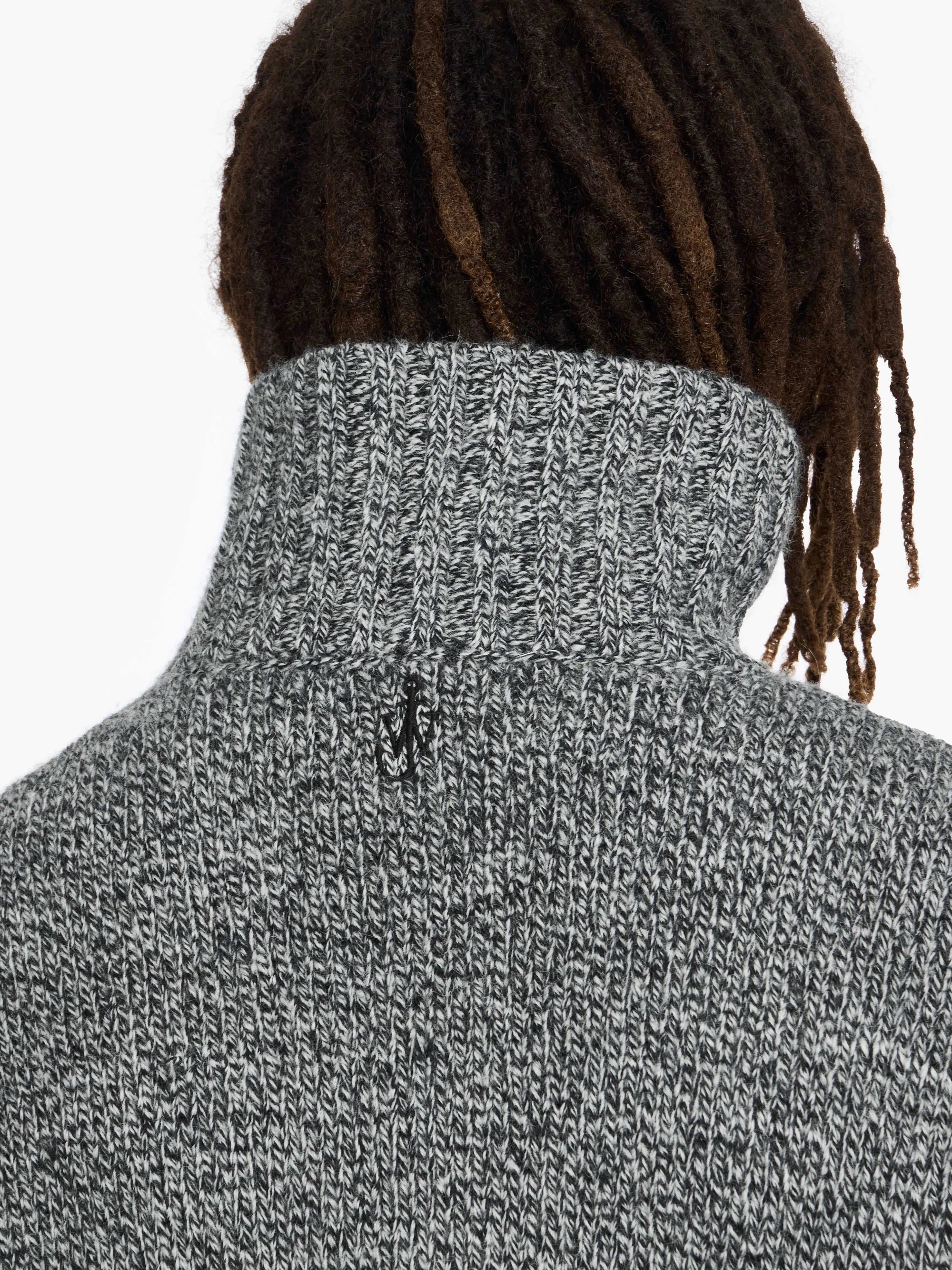 Person wearing a gray turtleneck sweater with a plain background