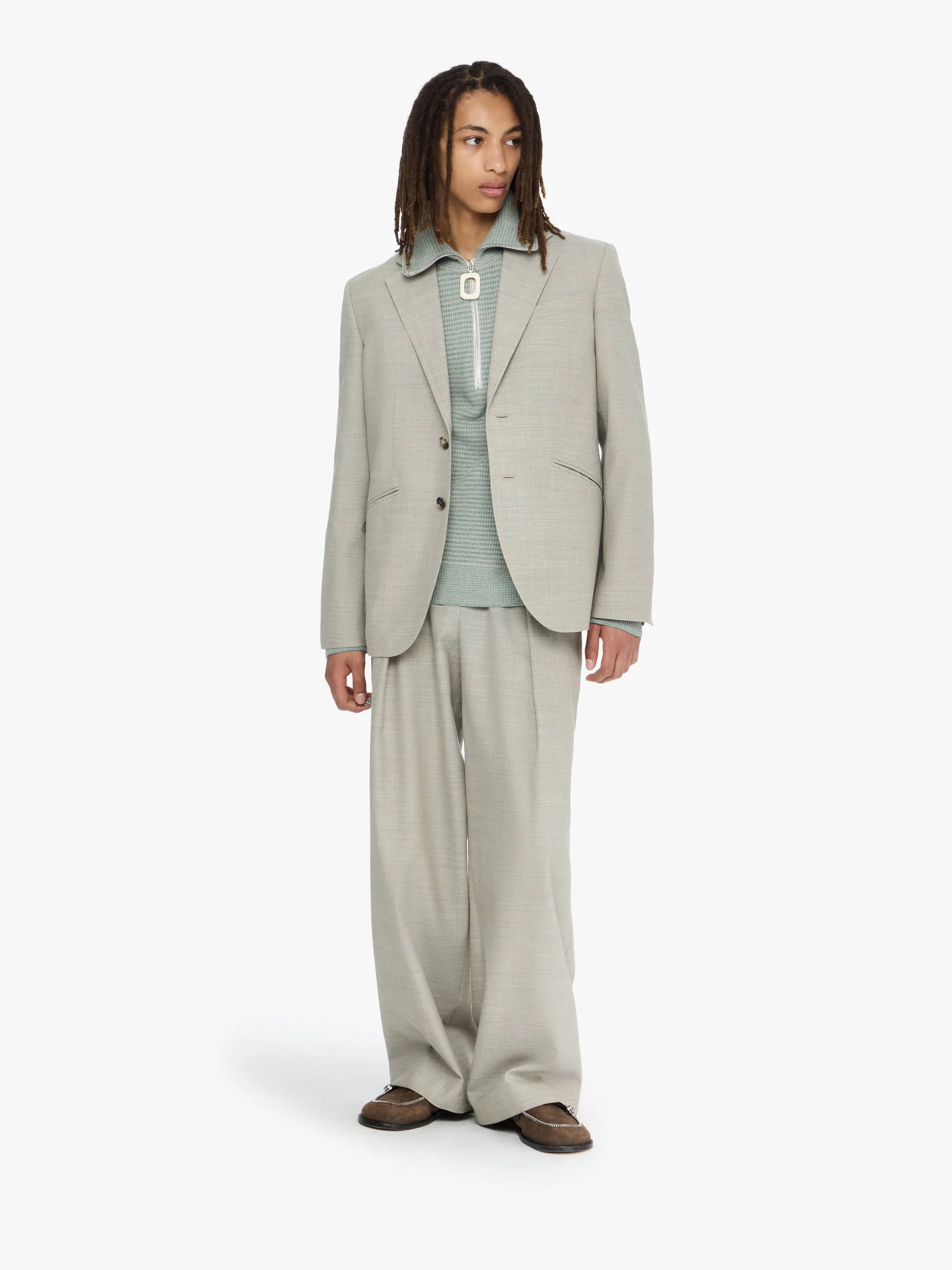 Person wearing a beige suit and green top on a white background