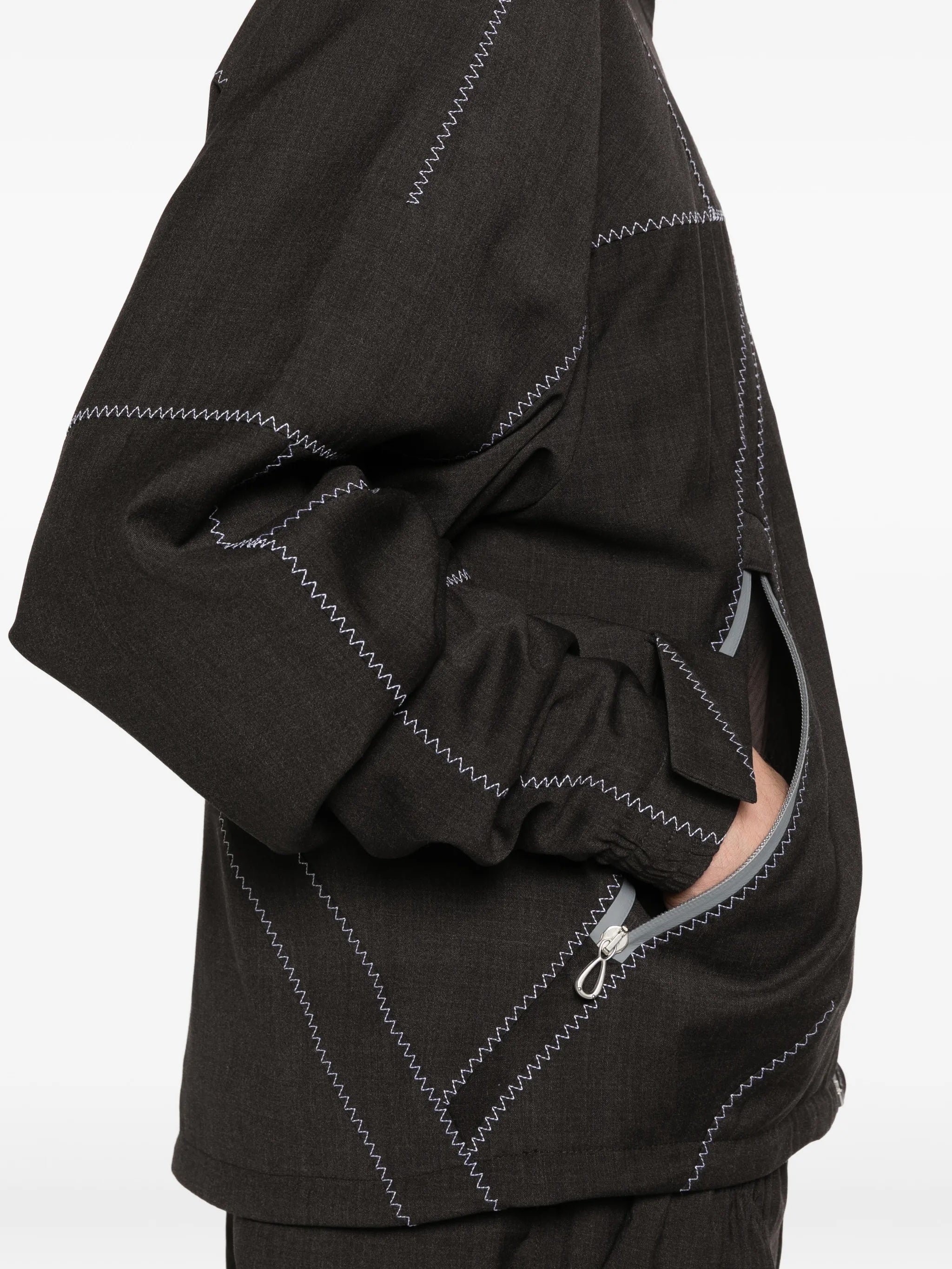 Side view of model wearing the dark brown jacket with white geometric contrast stitching from Kiko Kostadinov on a white background