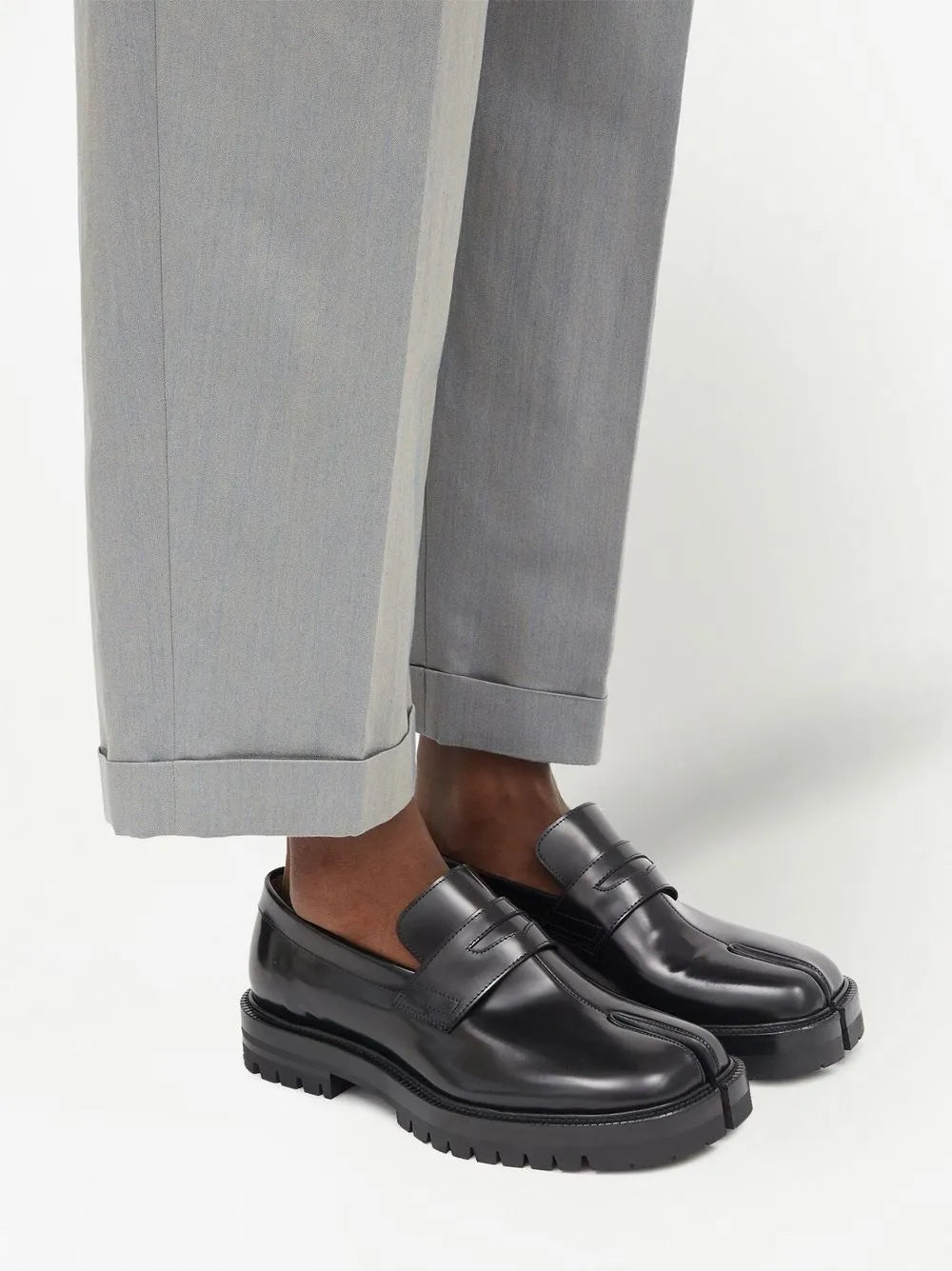 Black loafers worn with gray pants on a white background