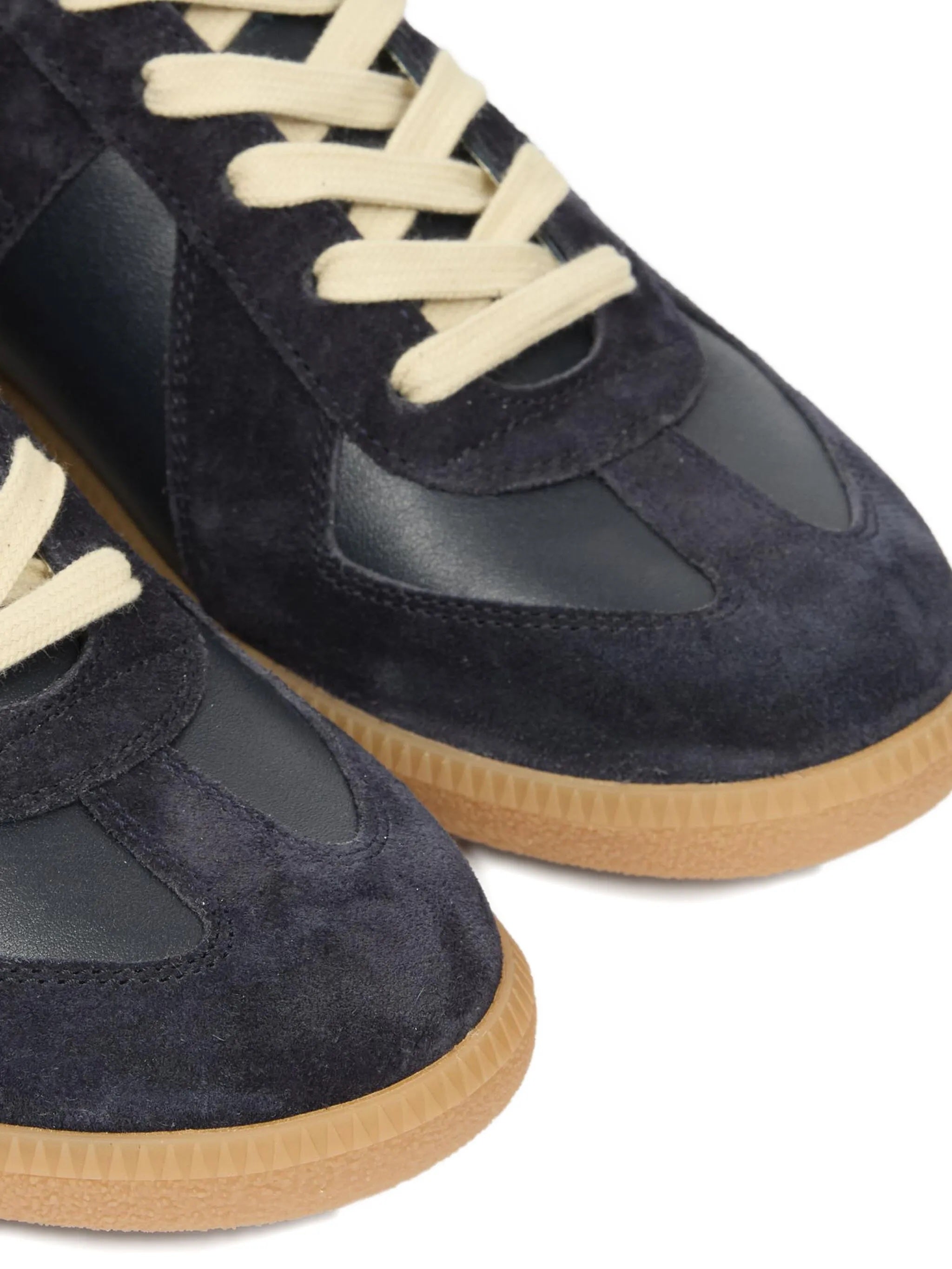 Close-up of dark navy blue leather sneakers with panel design and rubber soles on a white background