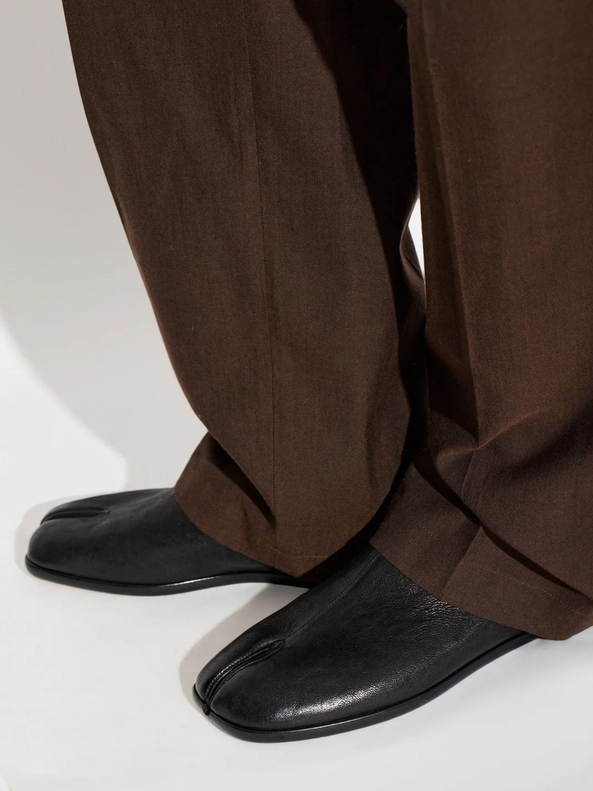 Maison Margiela Tabi Babouches in black styled with wide-leg brown tailored trousers, showing split-toe on foot