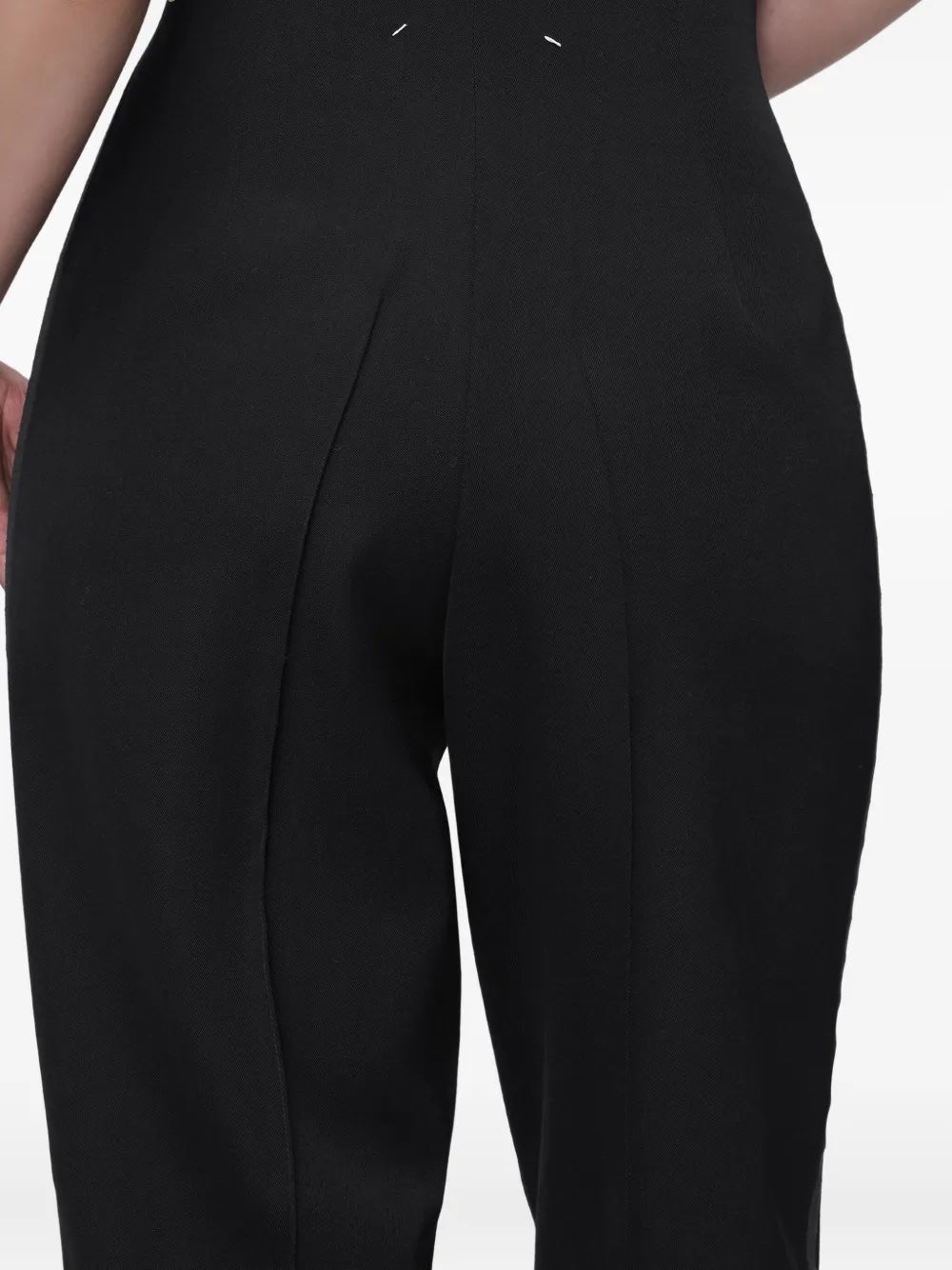 Close-up back view of the model wearing the black Maison Margiela pants, highlighting the signature four white stitches detail.