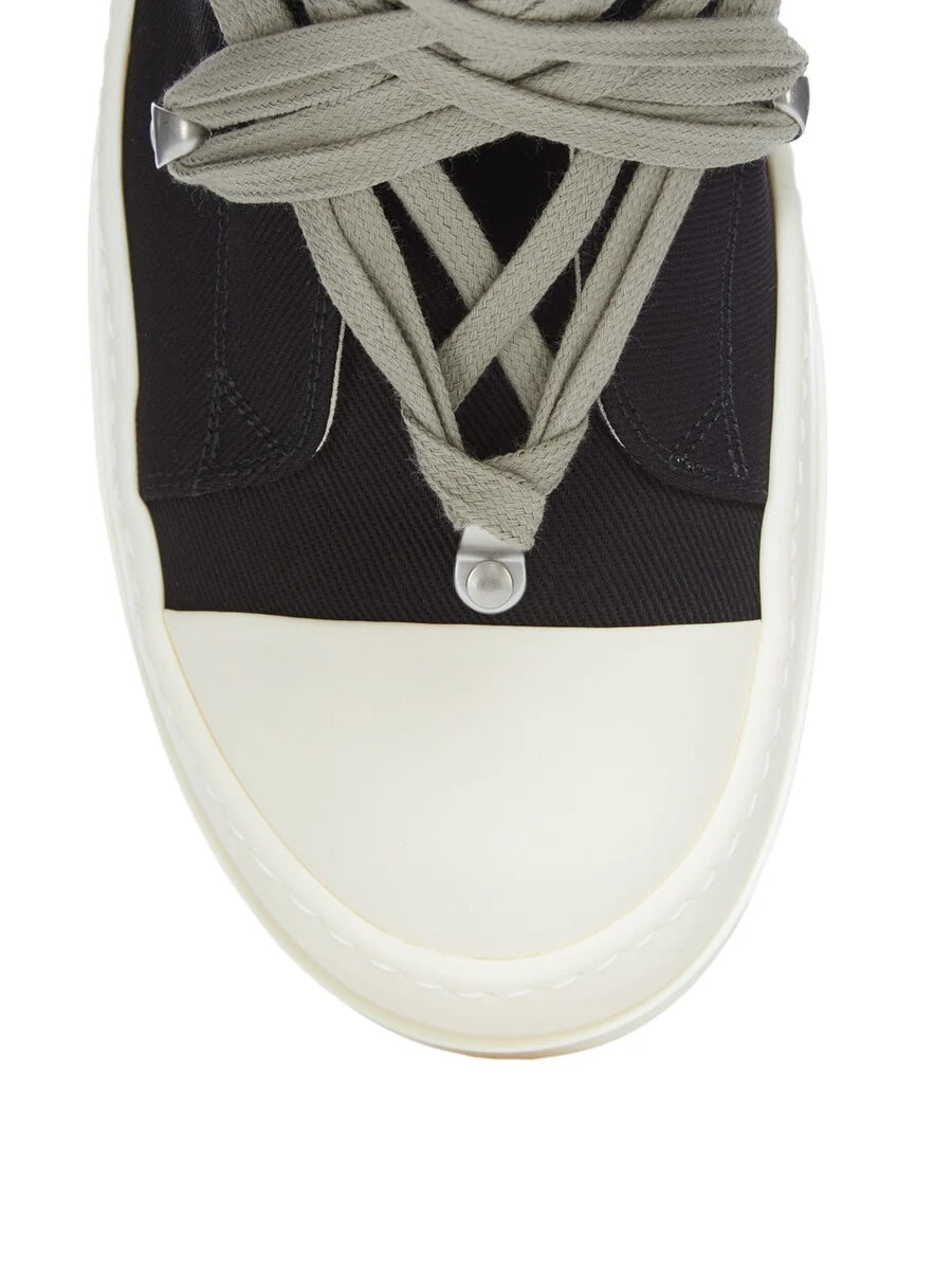 Close-up of Rick Owens DRKSHDW Megalace Sneaks showing pale grey wraparound lace detail with metal tips, black overdyed denim upper and milk white rubber toe cap